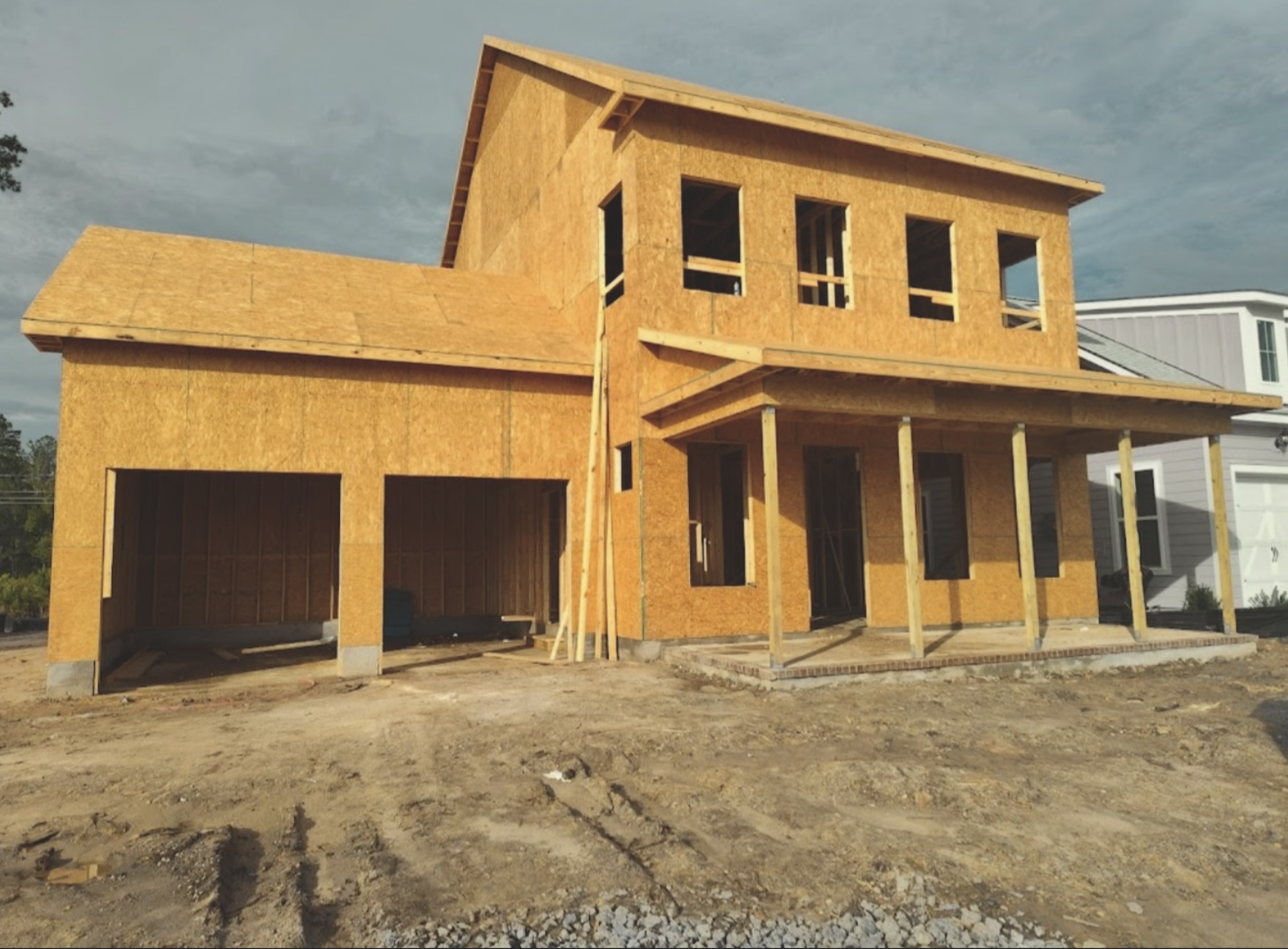 A house under construction with exposed wooden framing and no exterior siding, showing a garage and upper story.