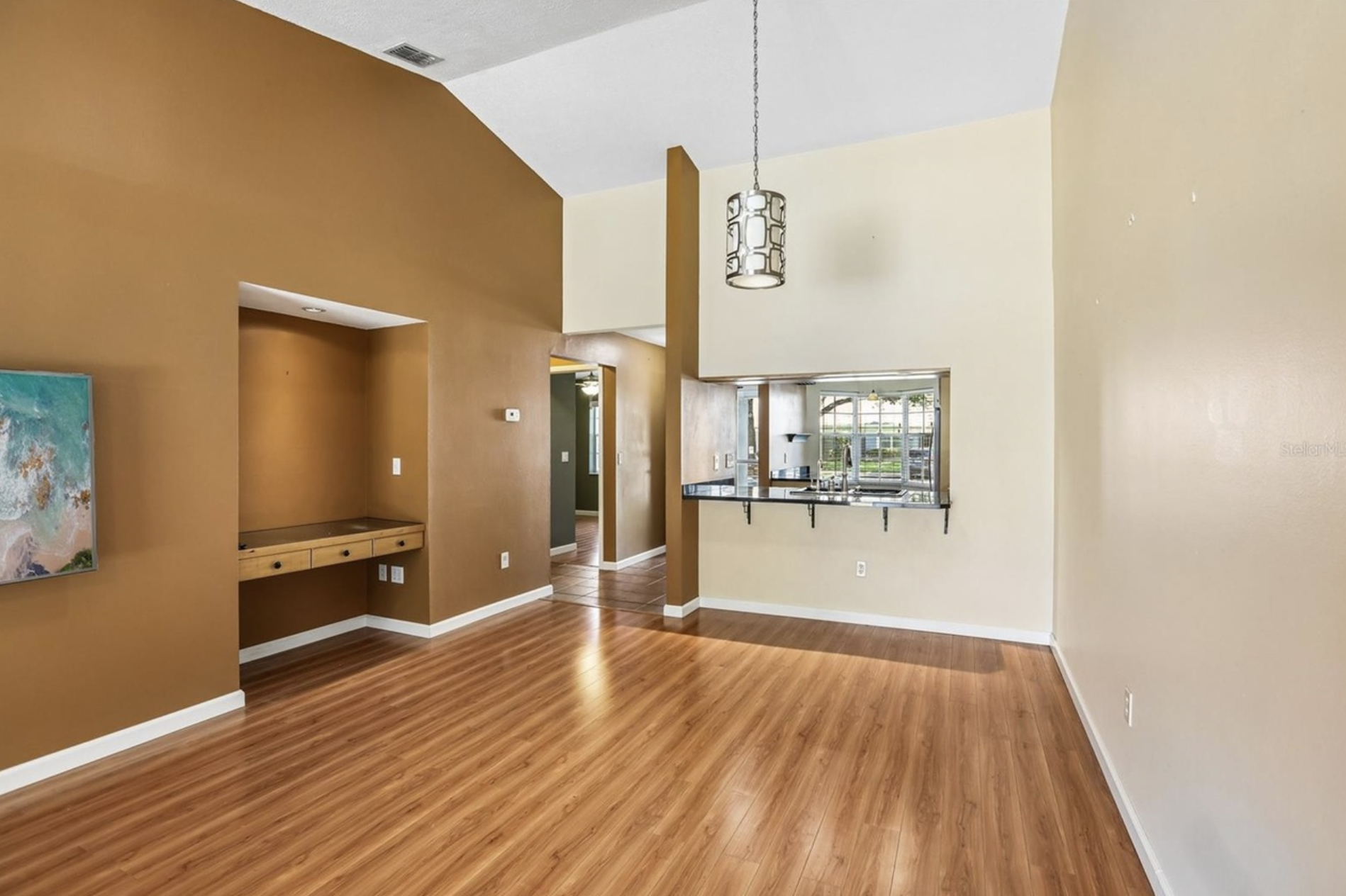 The dining and living room space has a high ceiling, skylight, laminate flooring, a wall mounted TV, and a built-in desk with electrical and USB outlets for working or homework providing both space and light.