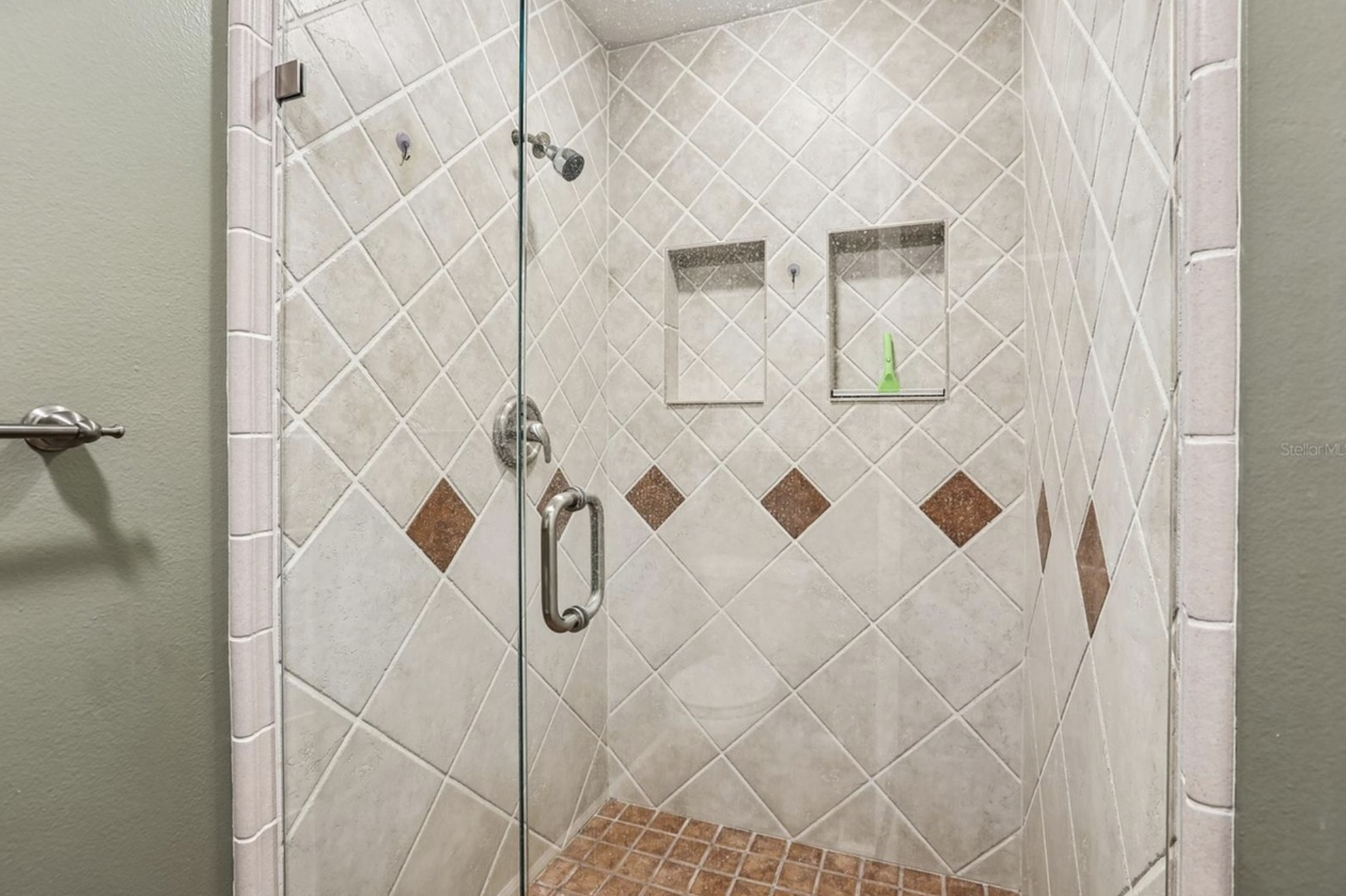 Bedroom #1 has a bathroom shower with beige and brown diamond-patterned tiles, built-in shelves, glass door, and showerhead.
