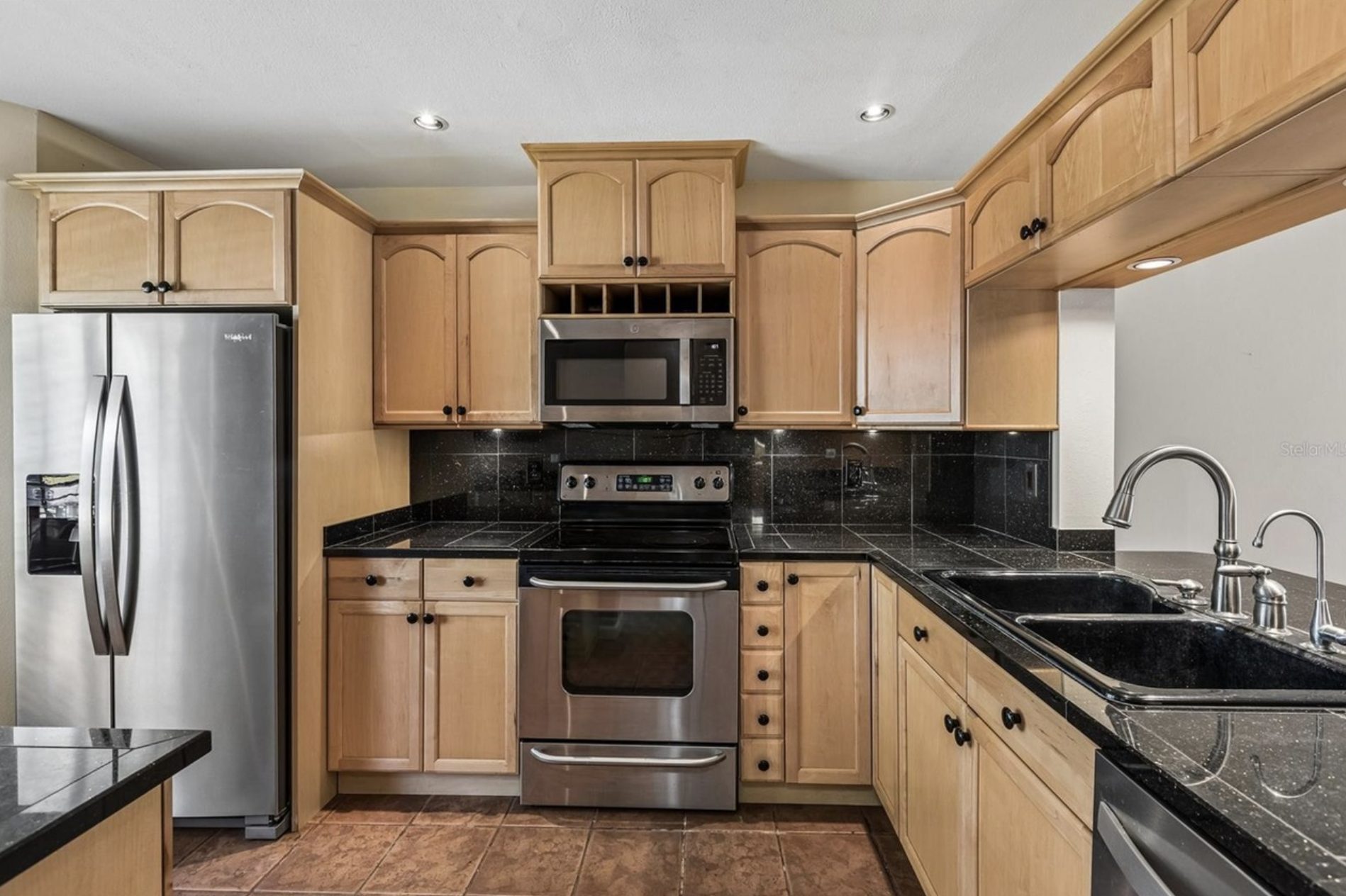 The kitchen is beautifully updated with modern wooden cabinets, black granite countertops, stainless steel refrigerator, microwave, stove, dishwasher, double sink, designer faucet.