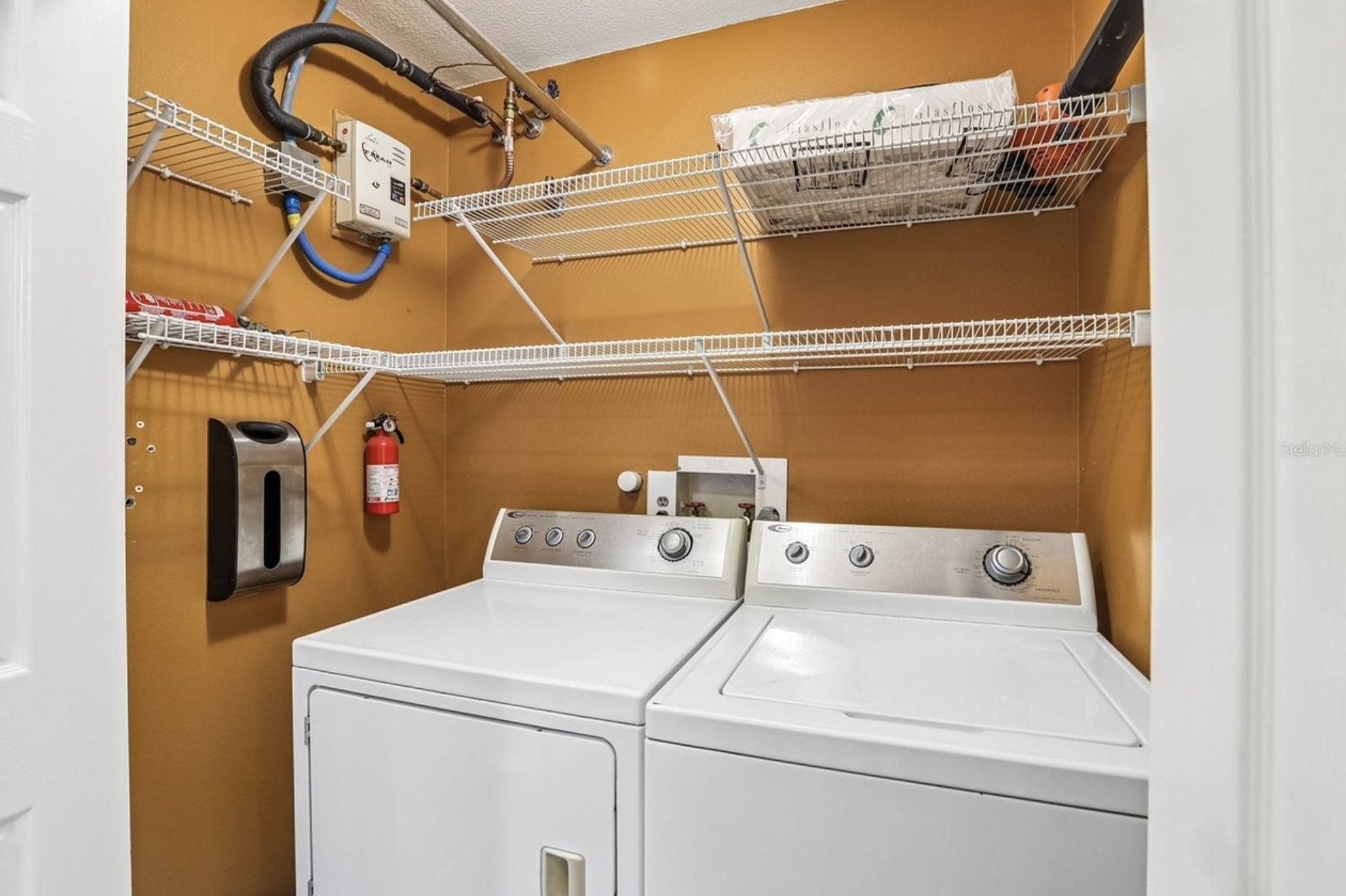 A laundry room with electric tankless water heater for instant hot water, storage, and a washer and electric dryer.
