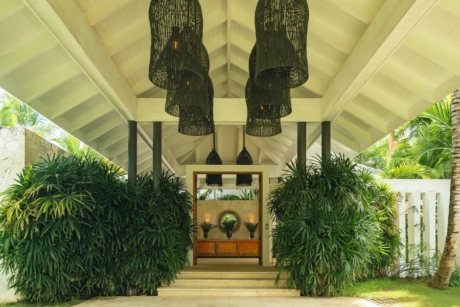 Entrance with hanging black pendant lights, surrounded by lush green plants, leading to an interior space with frosted glass doors and decorative plants.