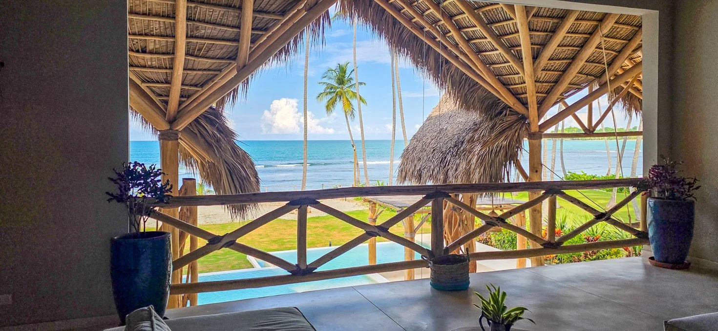 Beachfront terrace view through a thatched-roof pergola with ocean and palm trees at a kosher luxury villa, Dominican Republic