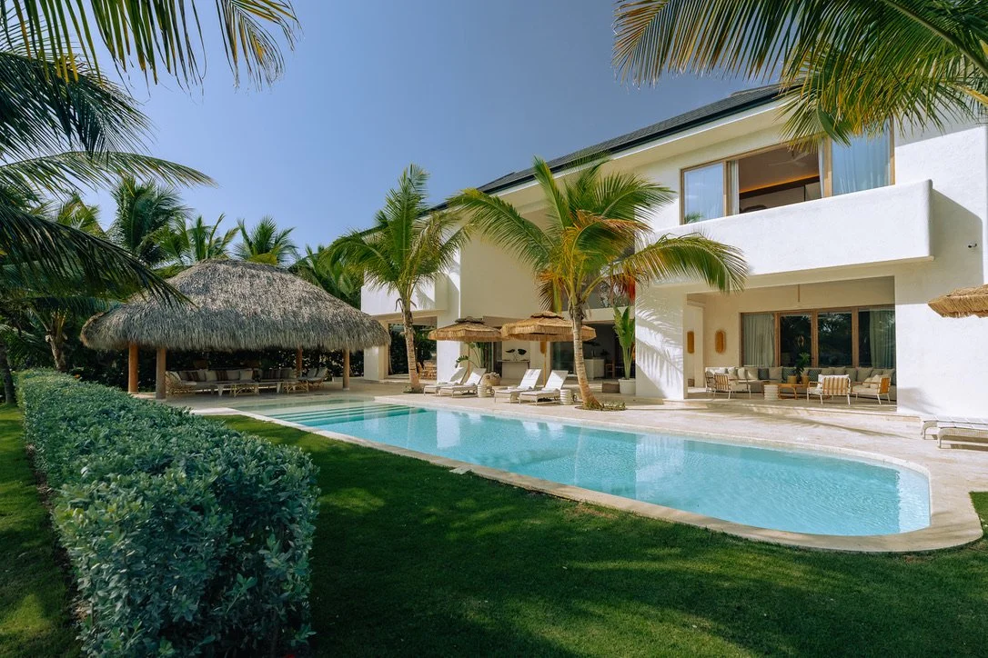 Luxury villa with a swimming pool, surrounded by palm trees, with outdoor lounge areas and tropical landscaping.