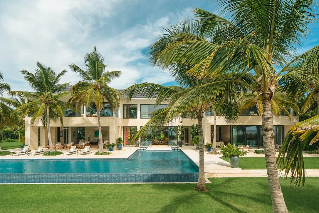 A luxury modern house with large glass doors, a swimming pool, and palm trees in a tropical setting.
