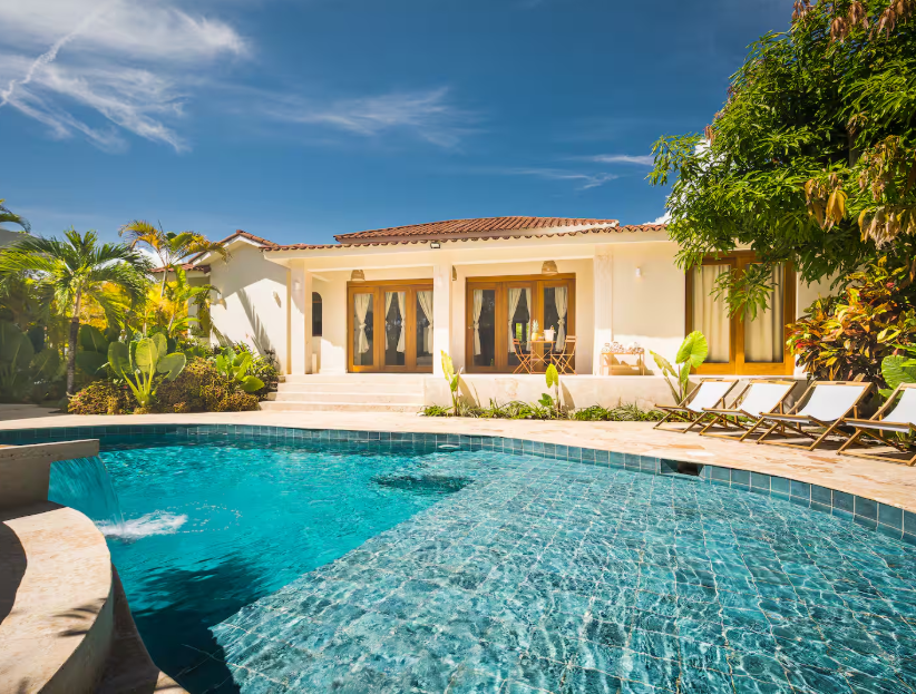 Luxury villa with a swimming pool, lounge chairs, and lush greenery under a clear blue sky.