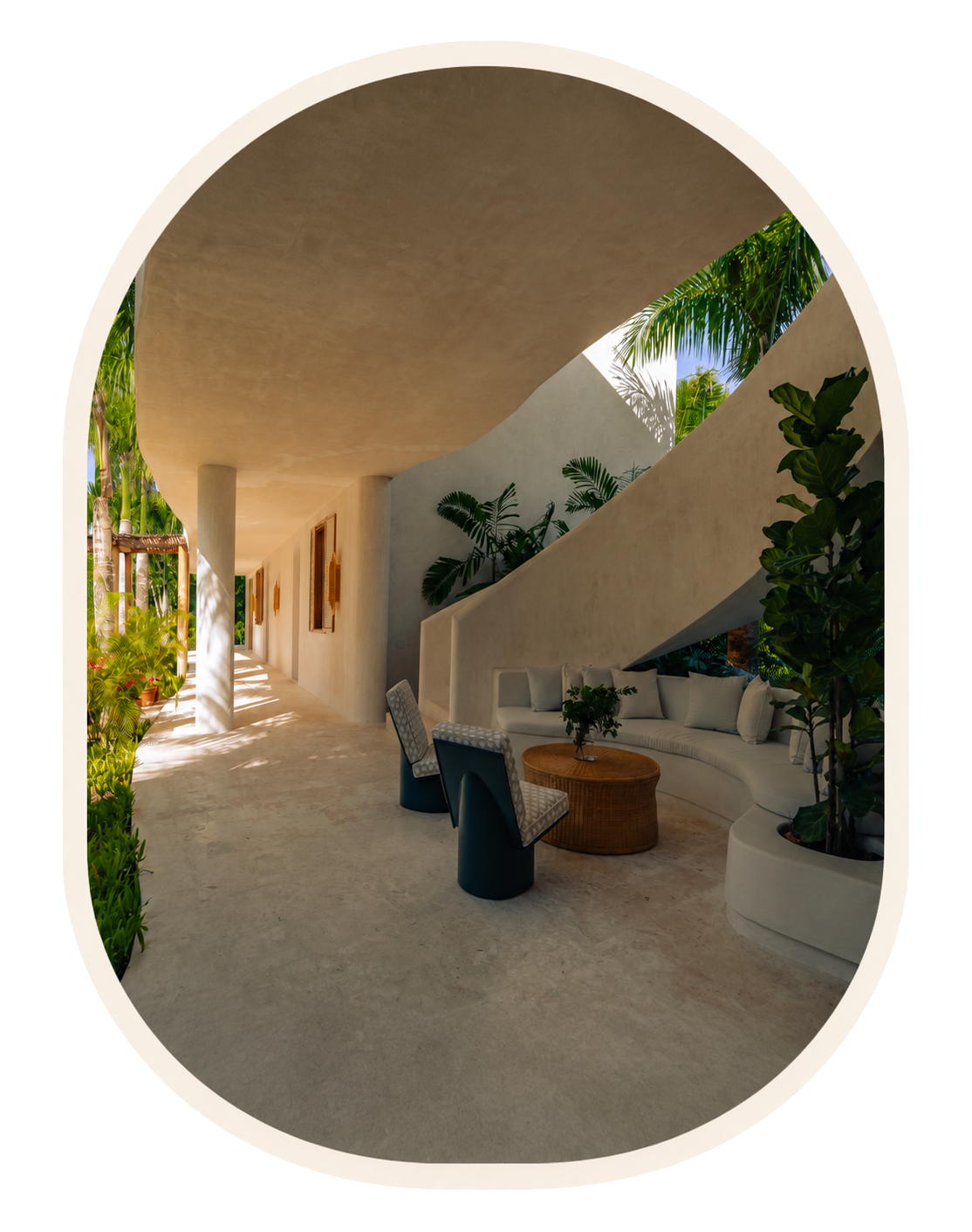 Open-air patio with curved white sofa, wicker coffee table, two armchairs, and tropical plants, under an arched ceiling.
