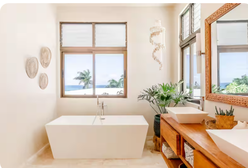 Freestanding bathtub beneath a window with ocean view, wood vanity, and coral wall decor at a kosher luxury villa, Dominican Republic
