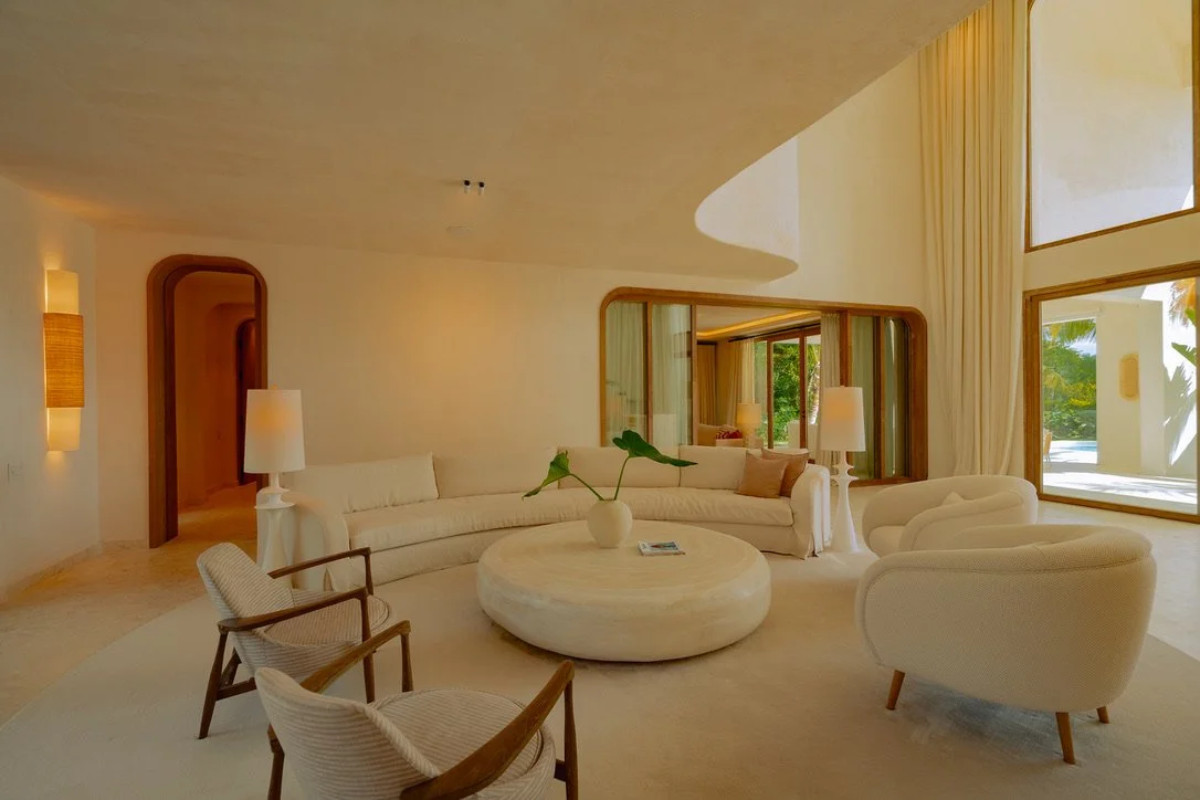 Living room with white sofas, armchairs, a circular coffee table, and large windows with curtains.