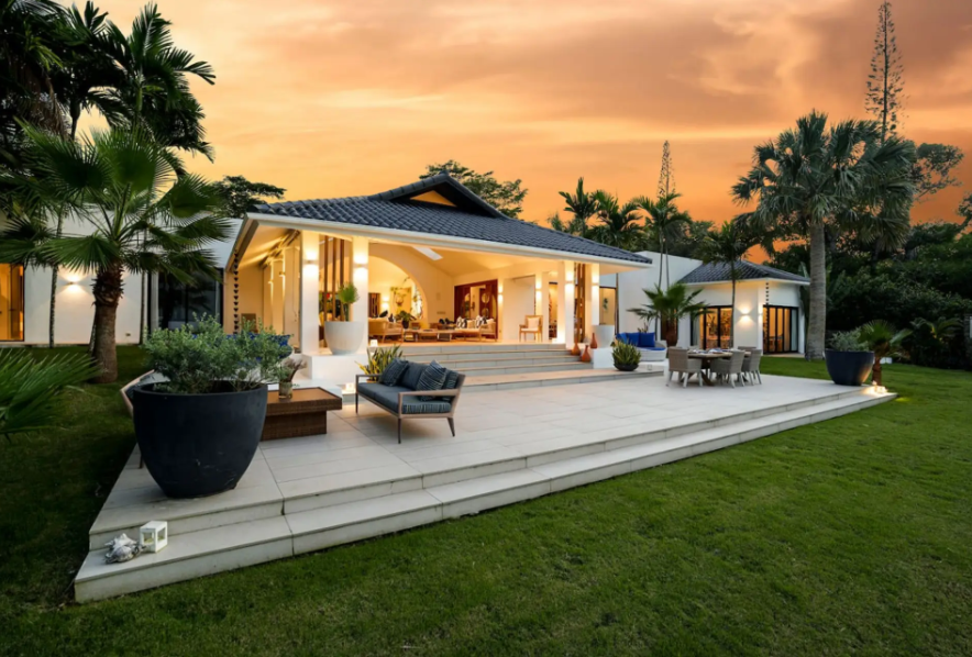 Single-story kosher luxury villa exterior at sunset with covered pavilion, patio seating, and lawn, Dominican Republic