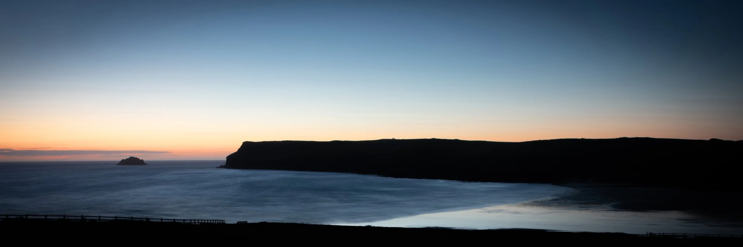 Sunset over Polzeath cliffs and ocean with a small island in the distance.