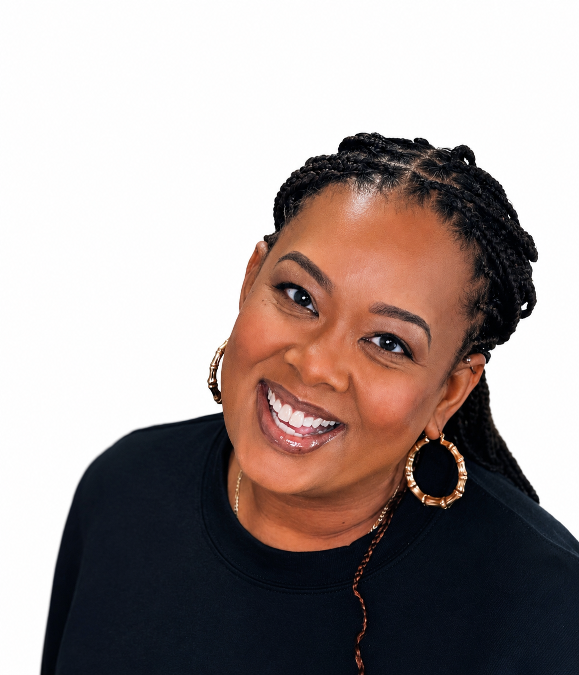 Smiling woman with braided hair, gold hoop earrings, and a black shirt against a white background.