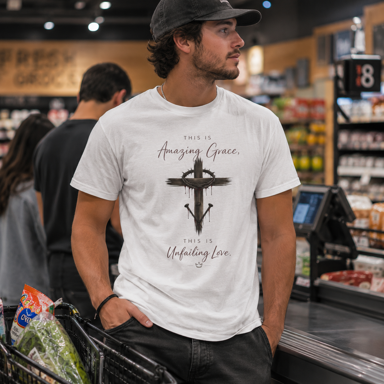 A young man in a white T-shirt with religious words and a cross graphic, standing at a store checkout counter.