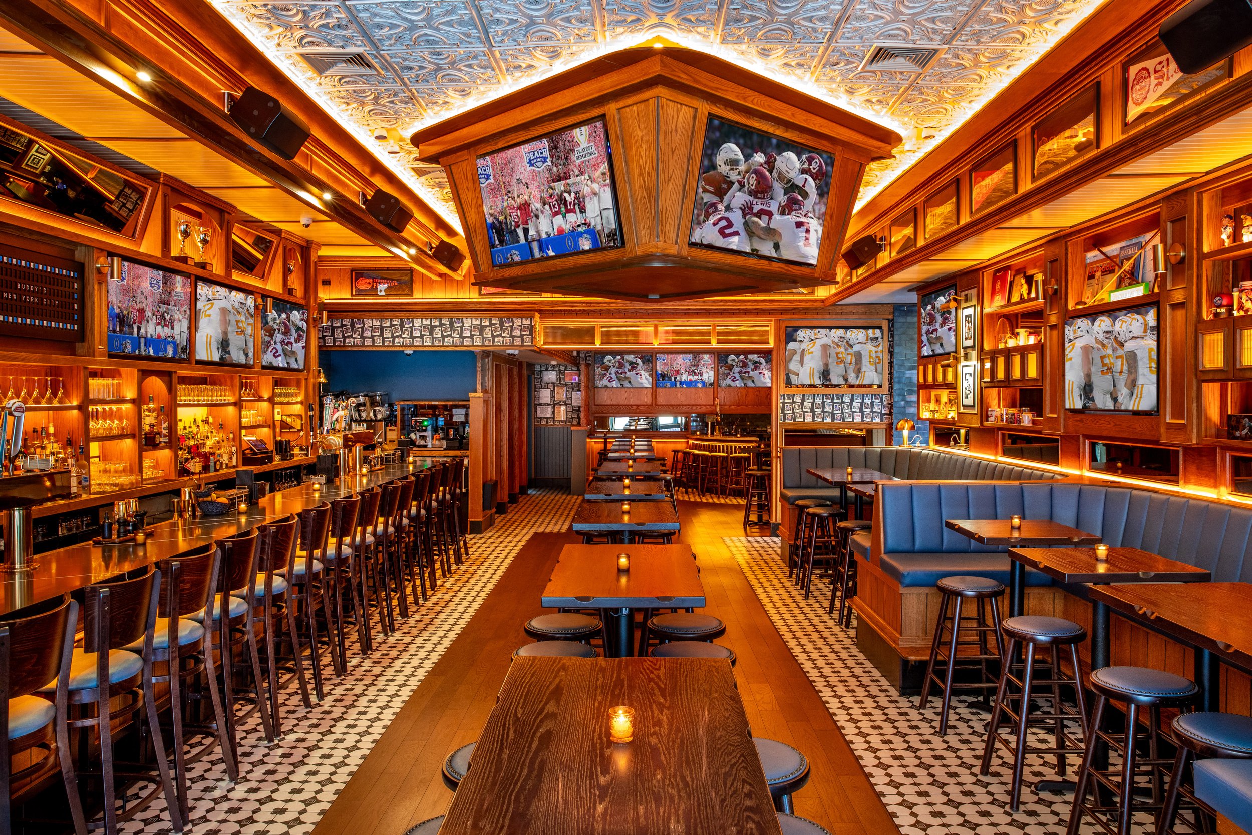 Interior view of a sports bar with multiple televisions showing football games, wooden furniture, bar area on the left, and candlelit tables.