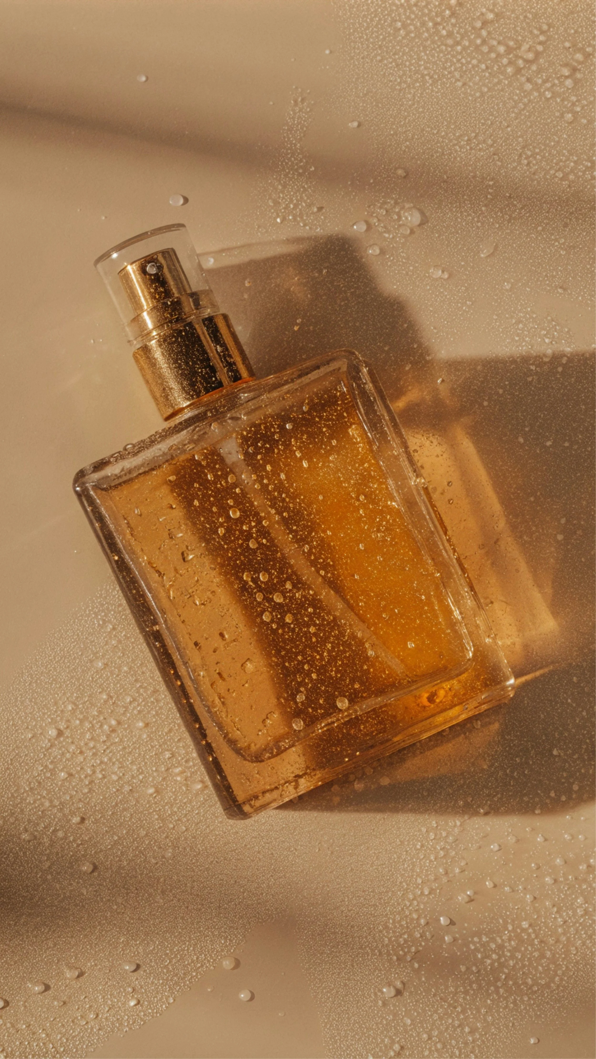 Frasco de perfume dorado con líquido dorado, sobre una superficie con gotas de agua.