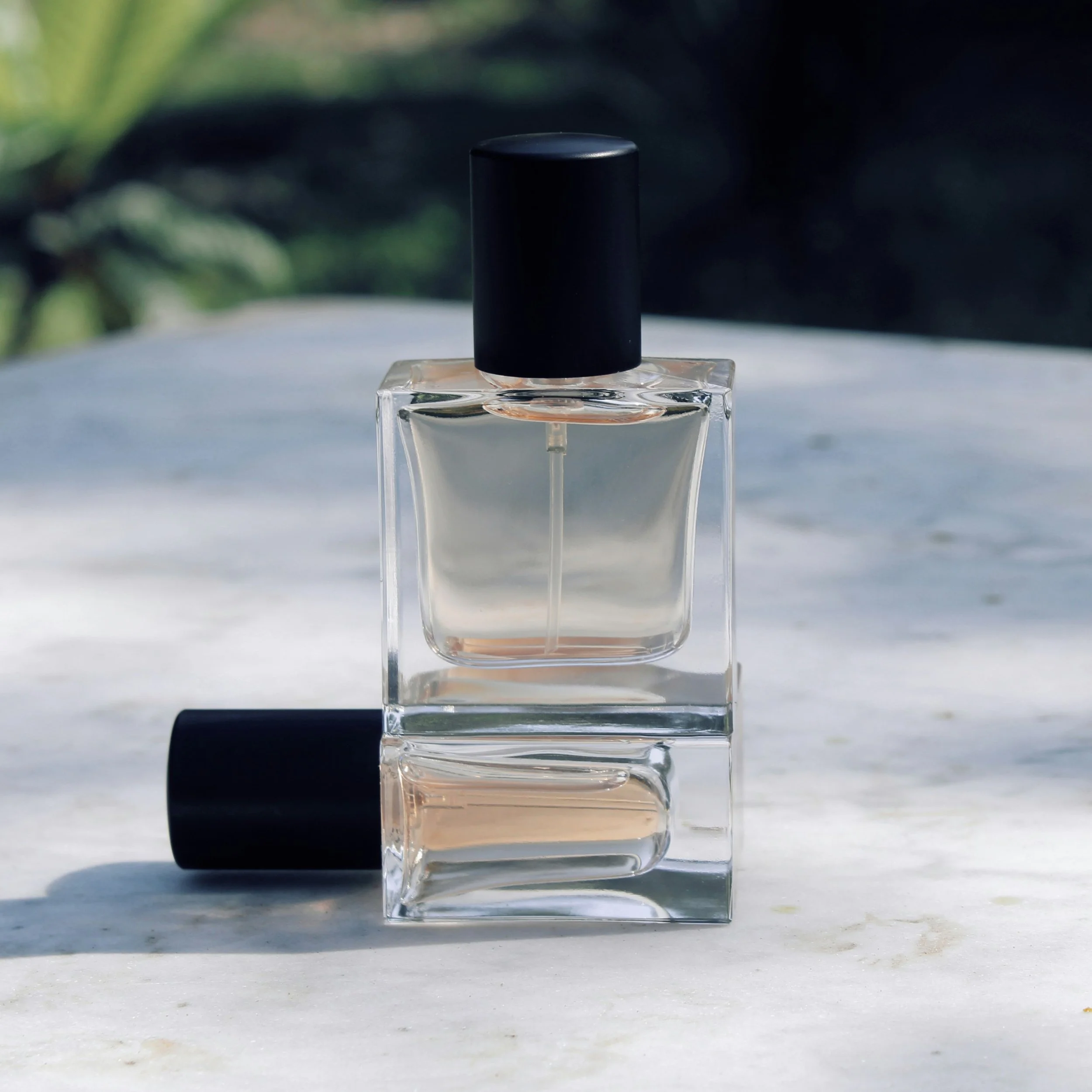 Frasco de perfume con tapa negra y cuerpo transparente, colocado sobre una superficie clara con fondo oscuro y difuso.