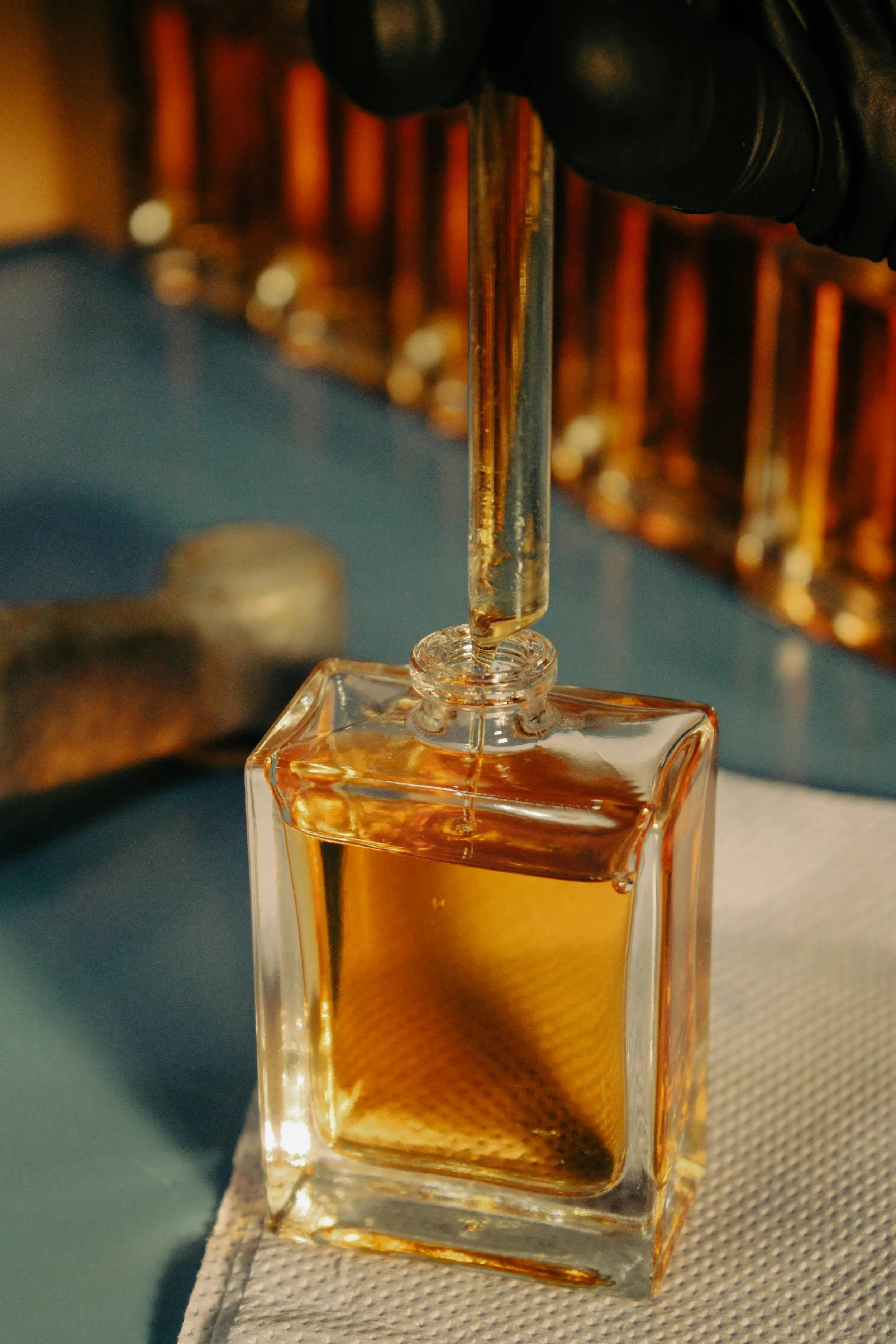 Frasco de perfume transparente con líquido dorado en una superficie gris con fondo borroso.