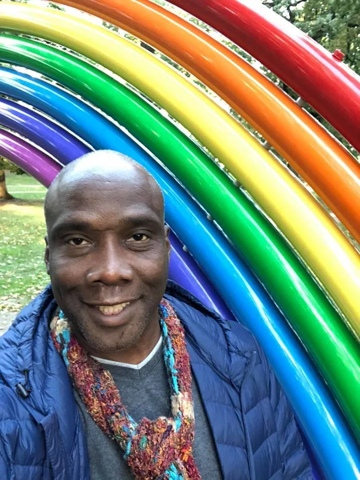 Austin Nation smiling in front of a rainbow sculpture celebrating LGBTQ Pride