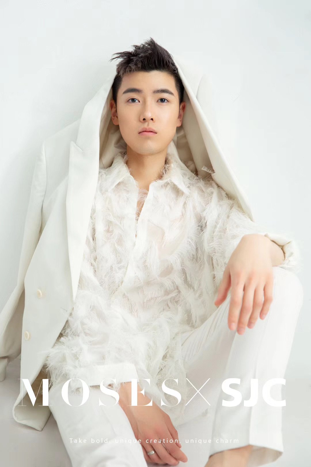 A young man with short dark hair and light skin wearing a white feathered shirt and white pants, sitting against a plain white wall, with the text 'MOSE SJC' at the bottom of the image.