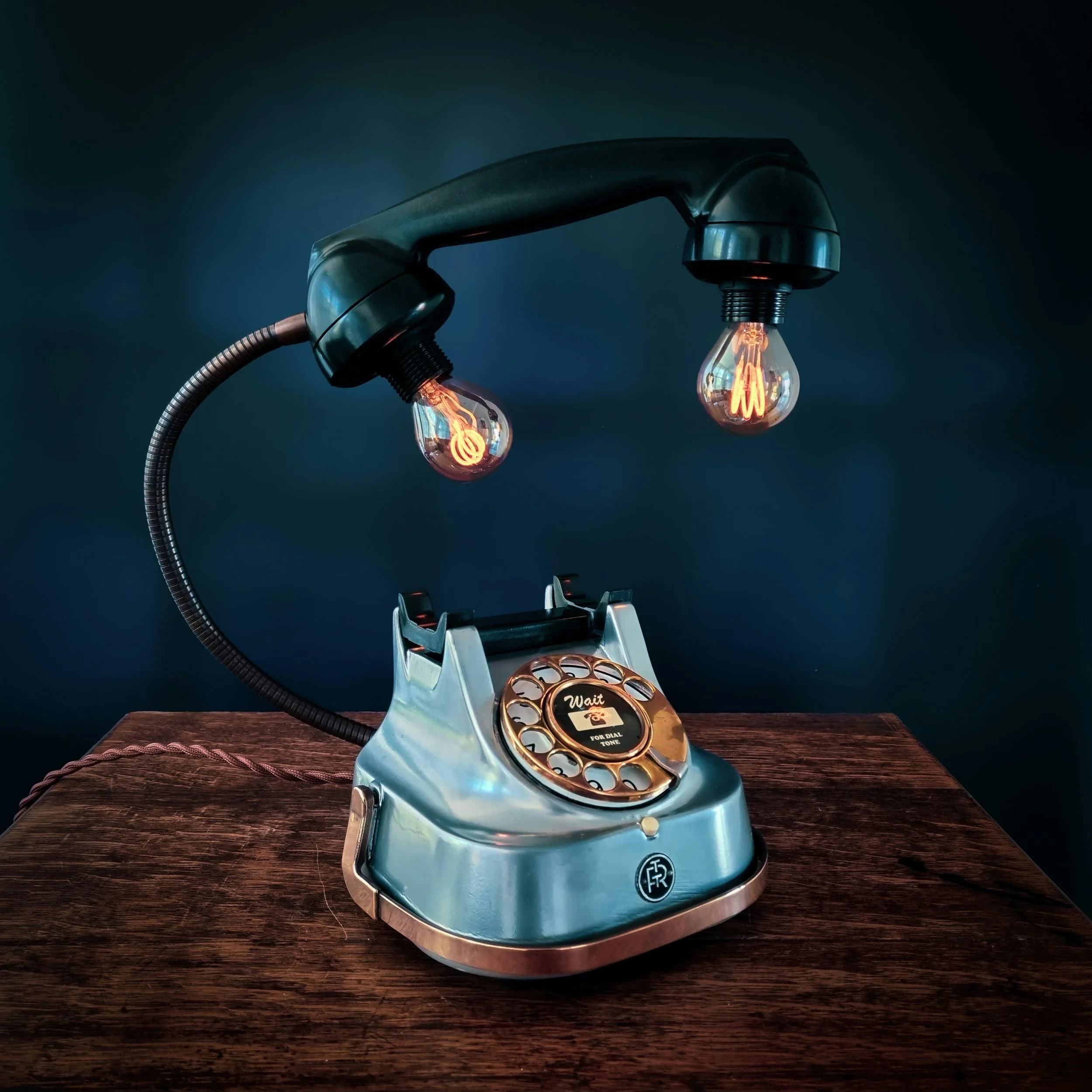 An antique rotary telephone with a metallic finish and a circular dial, placed on a wooden surface against a dark background.