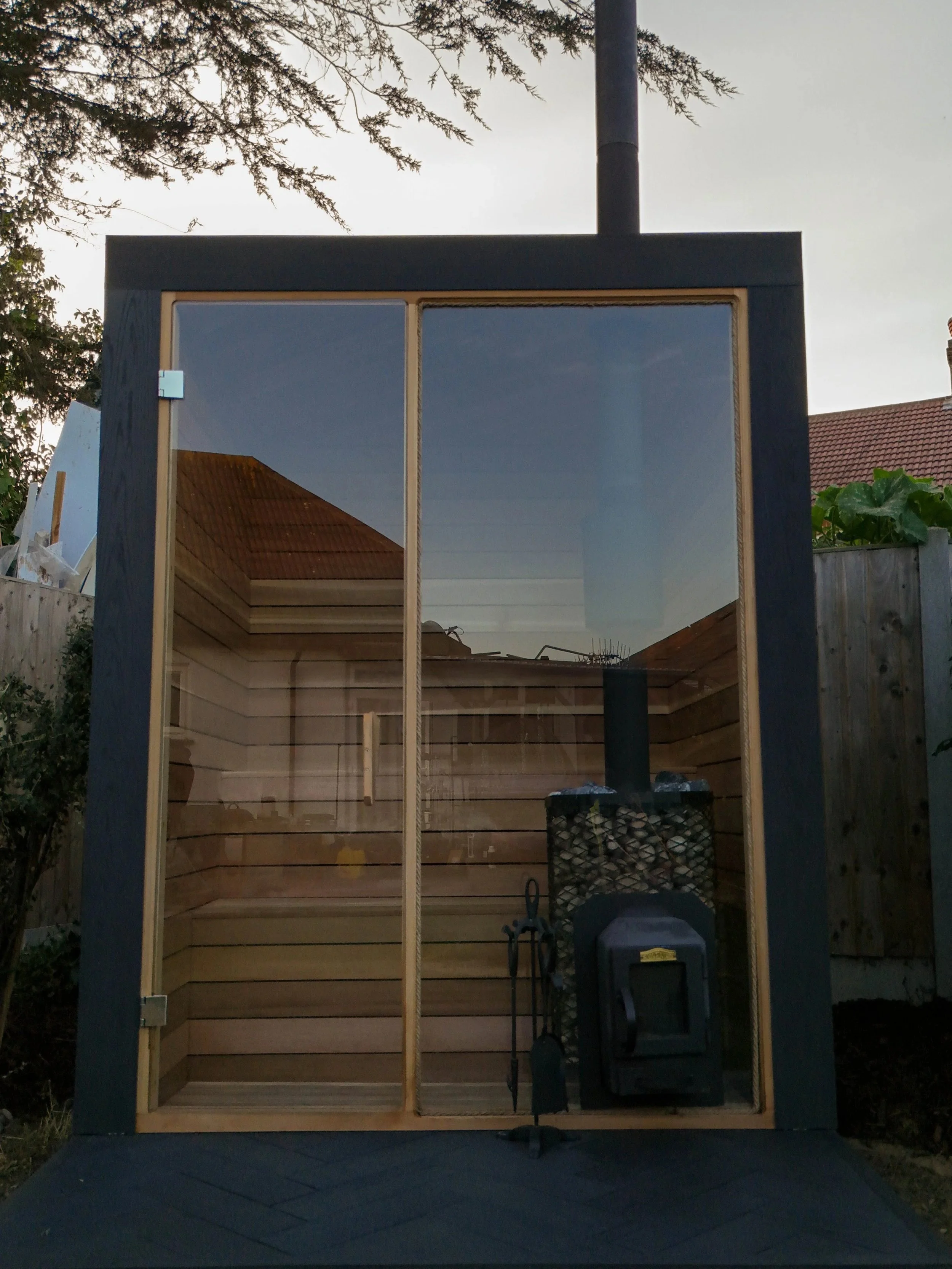 An outdoor woodworking or shed building area with a mostly completed wooden frame and a mirror reflecting a shed roof.
