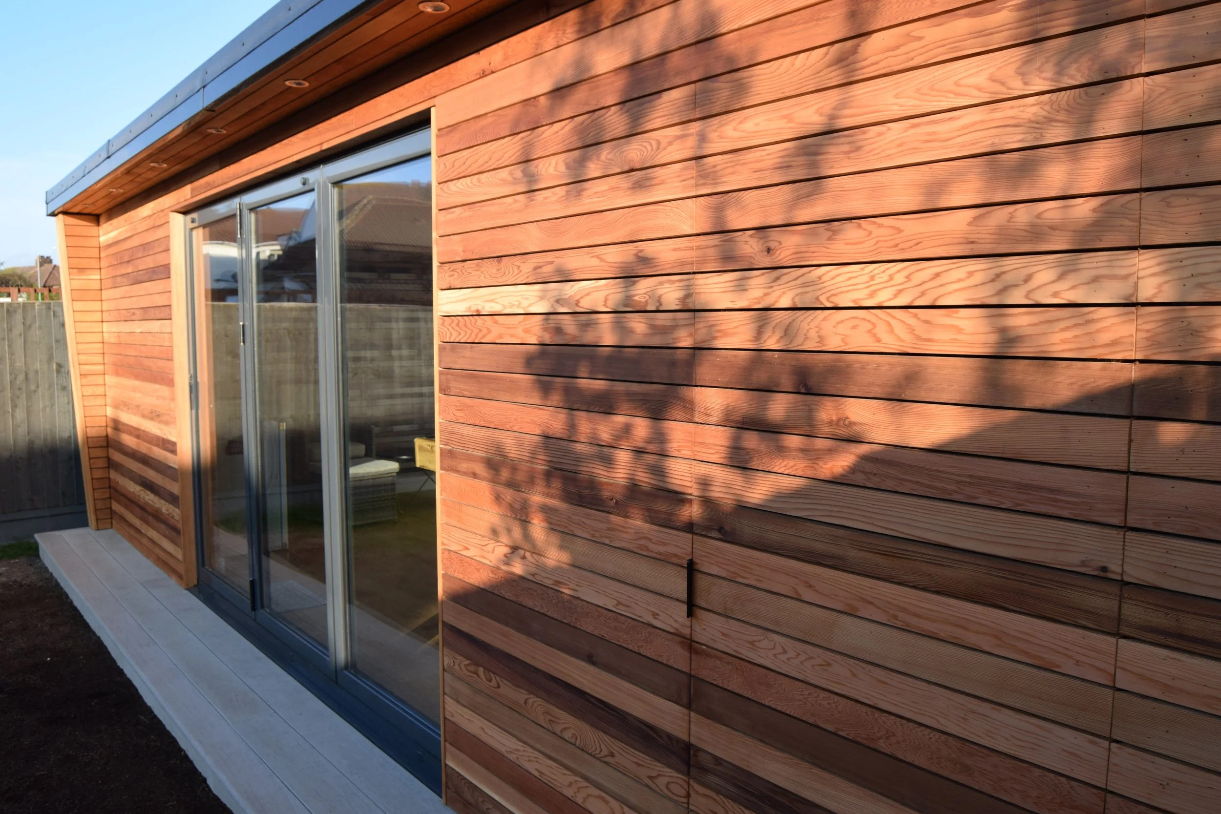 Exterior view of a modern house with wooden siding and large glass sliding doors, situated on a white concrete porch.