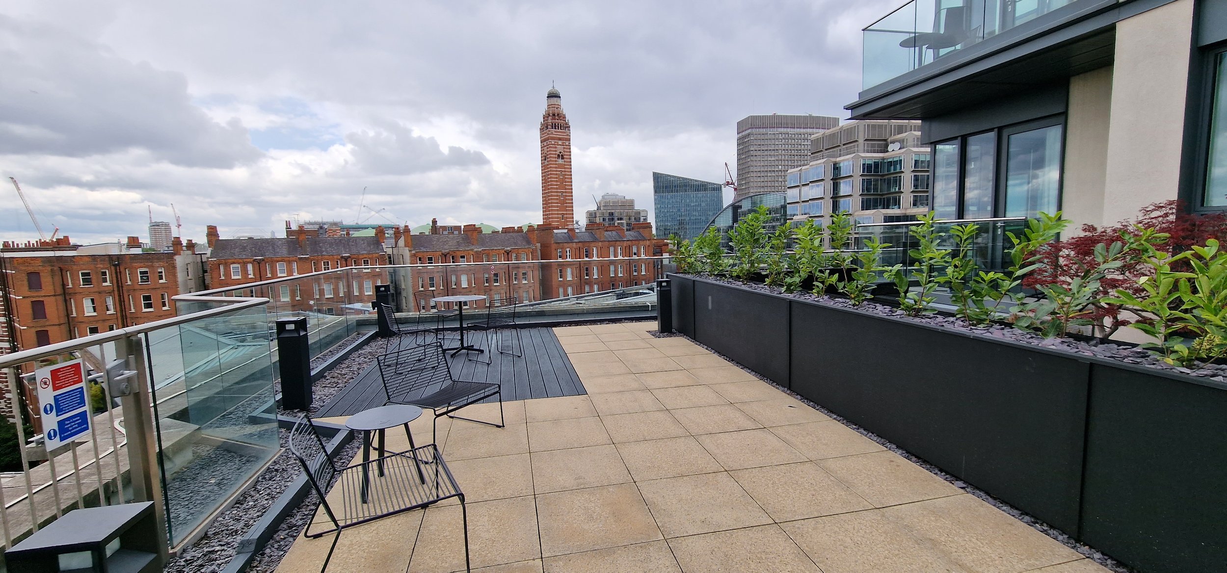 Rooftop terrace with table, chairs, and potted plants overlooking cityscape with historic and modern buildings