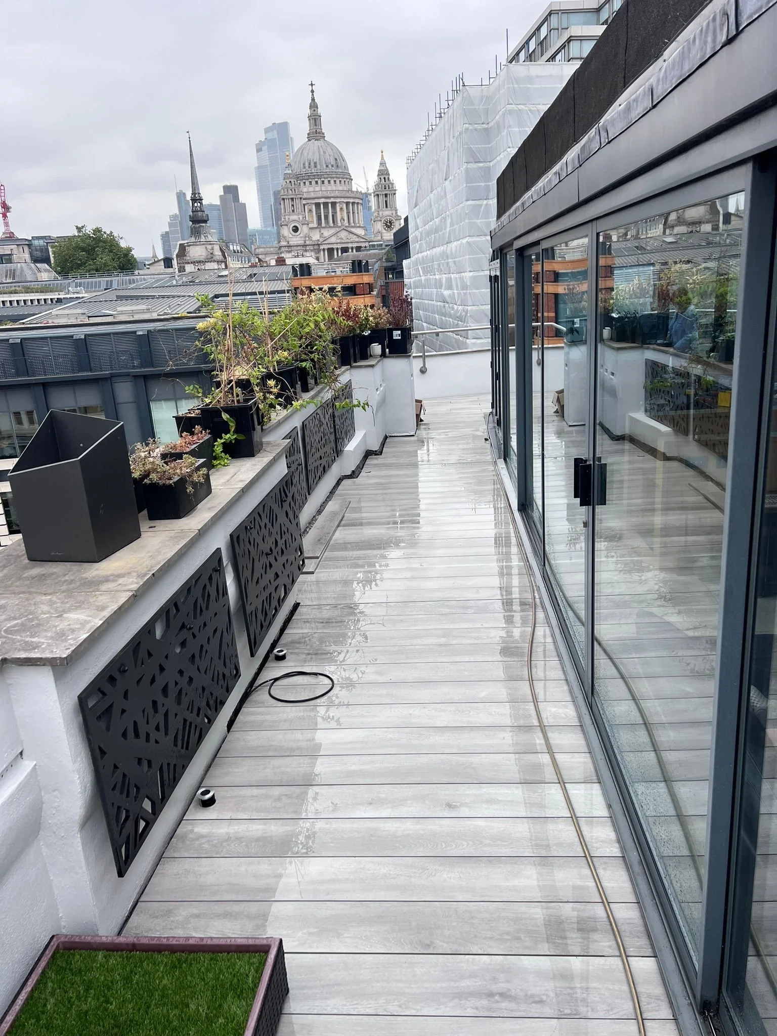 City rooftop terrace with potted plants, glass sliding door, and view of historic and modern buildings in London, UK.