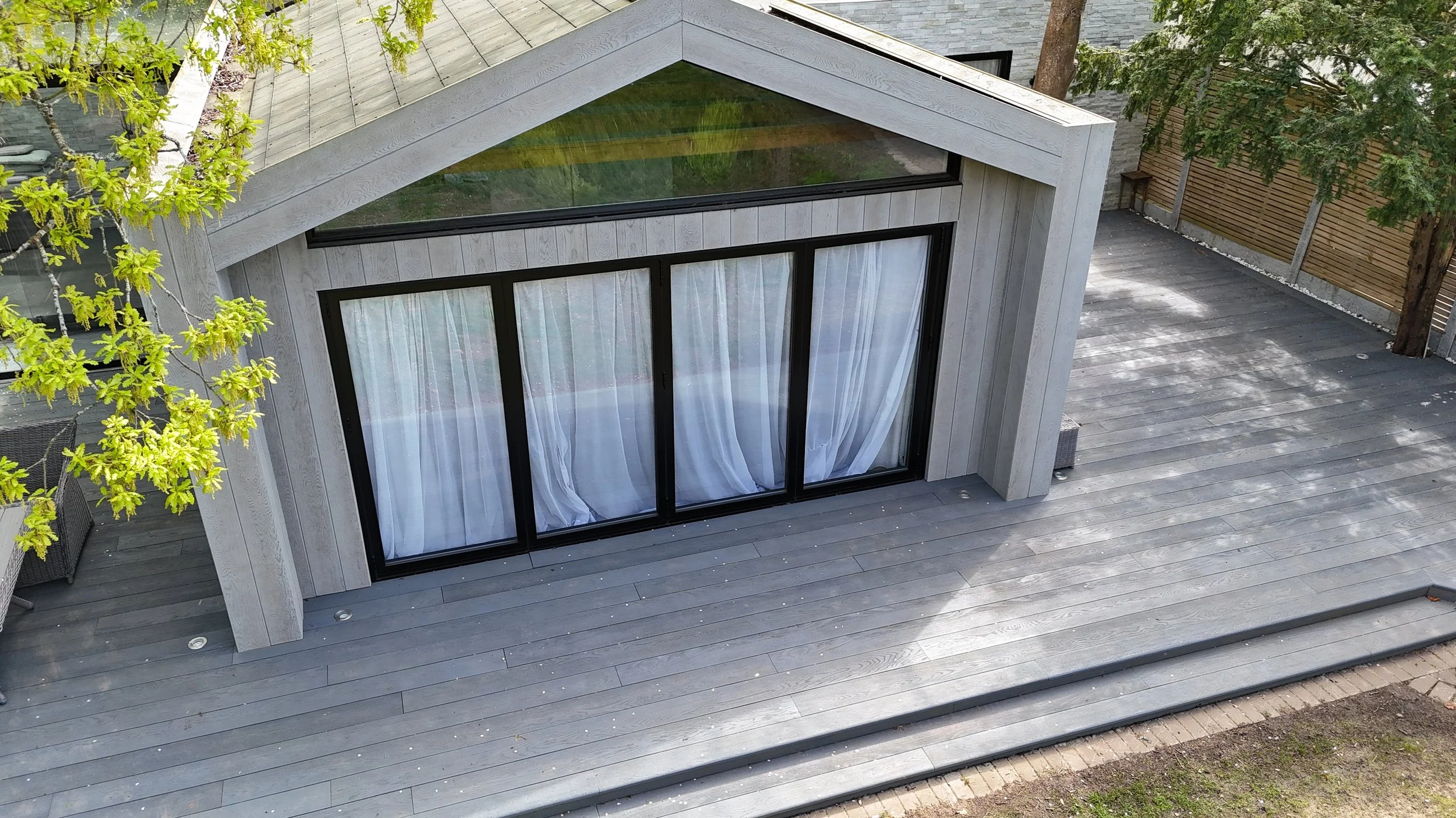 Modern house with large sliding glass doors and a wooden deck, surrounded by trees.
