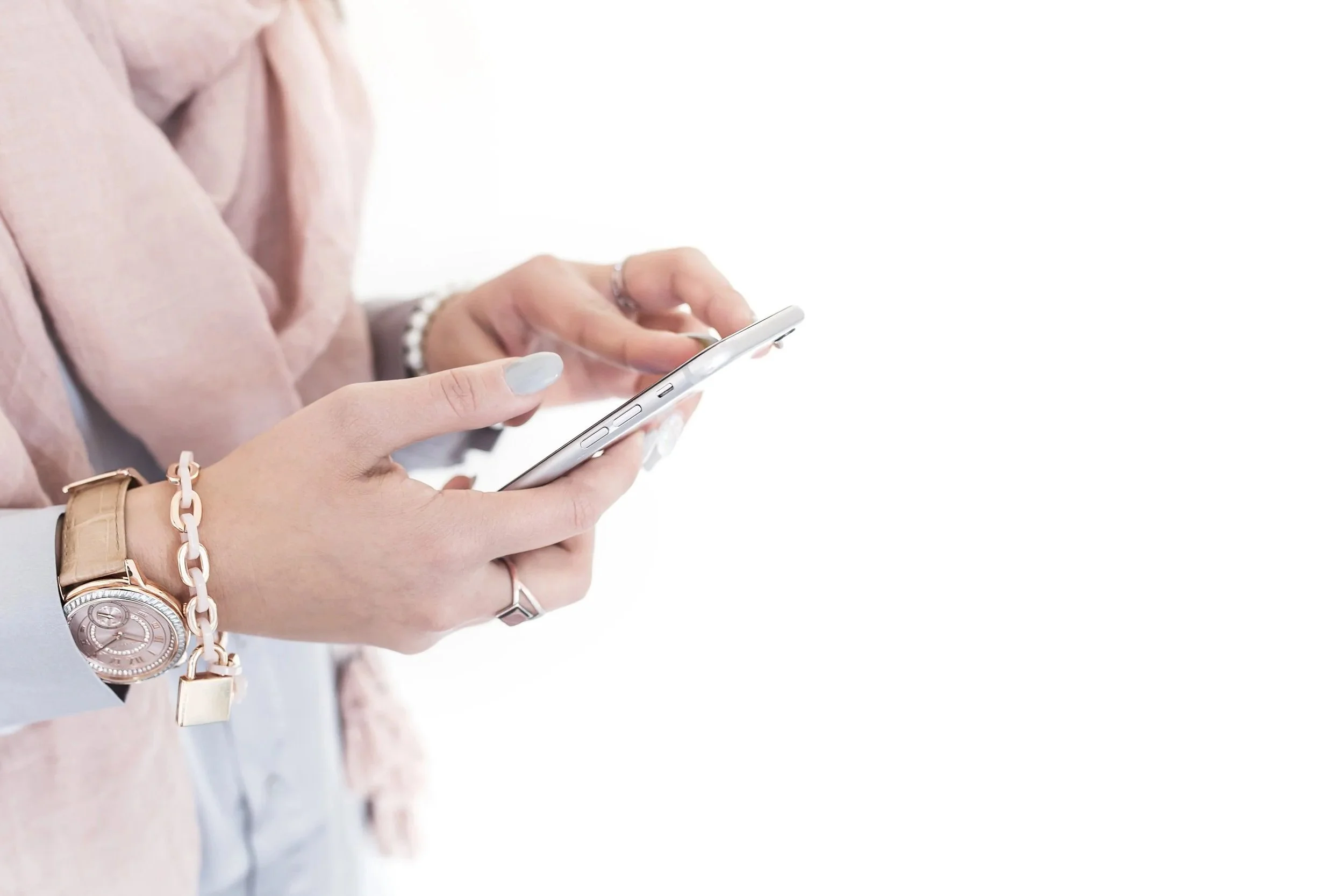 Person using a smartphone, wearing a watch, rings, and a bracelet, with a blurred business suit sleeve visible.