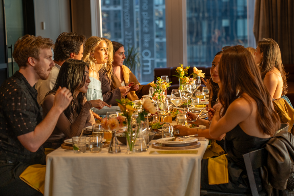 People sitting at a dinner party table with flowers and glassware in a modern restaurant.