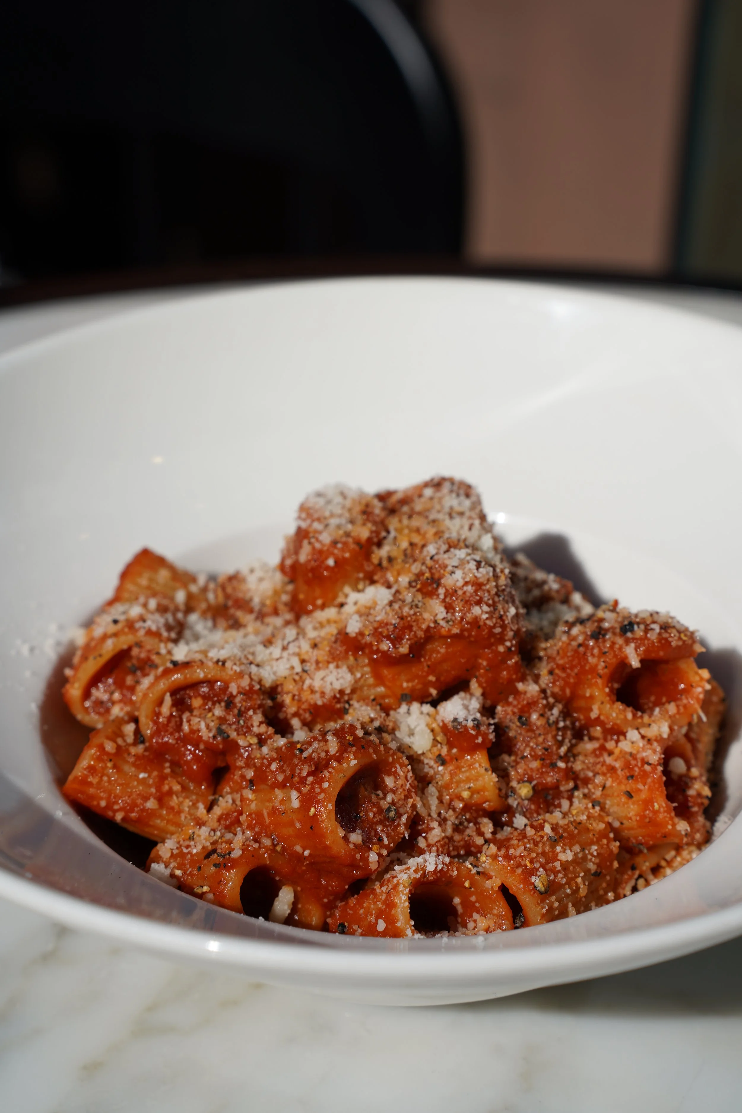 A bowl of cooked pasta with meat sauce, topped with grated cheese and black pepper.