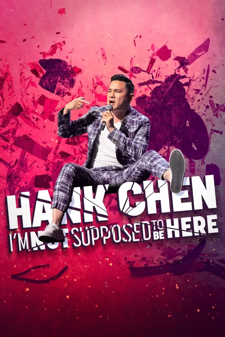 A man wearing a plaid suit is sitting cross-legged and speaking into a microphone on a colorful, dynamic background with shattered shapes and bold text. "Hank Chen: I'm Not Supposed to Be Here"