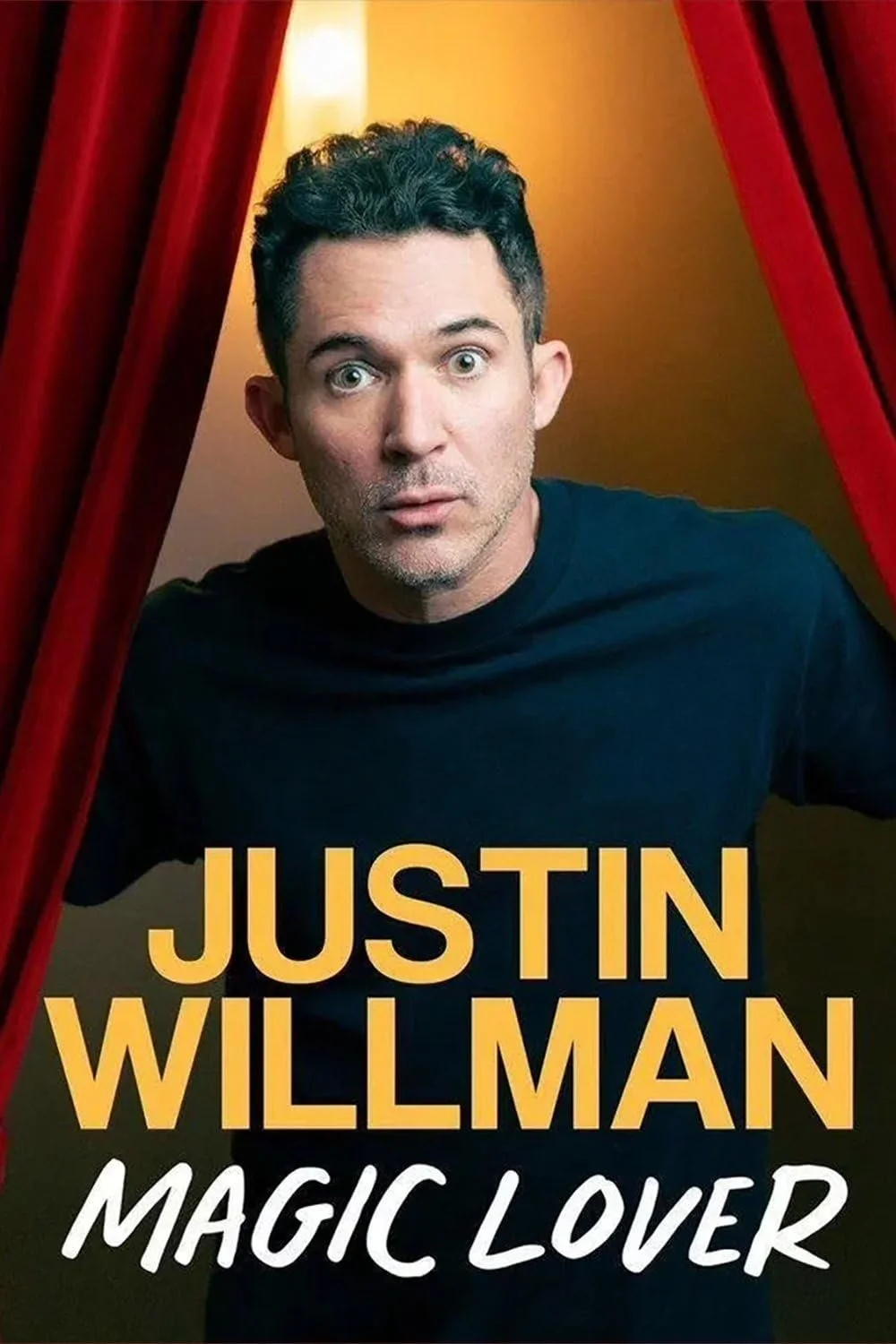 Promotional poster for comedy special "Magic Lover" by Justin Willman, featuring a photograph of a man with short, dark curly hair, wearing a black shirt, looking surprised with wide eyes, framed by red curtains.