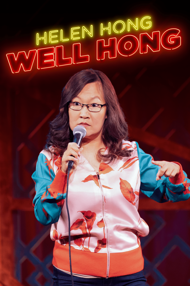 A woman with glasses and long dark hair holding a microphone, standing in front of a neon sign that reads "Helen Hong Well Hong". She is wearing a colorful jacket with a floral pattern and gesturing with her right hand.