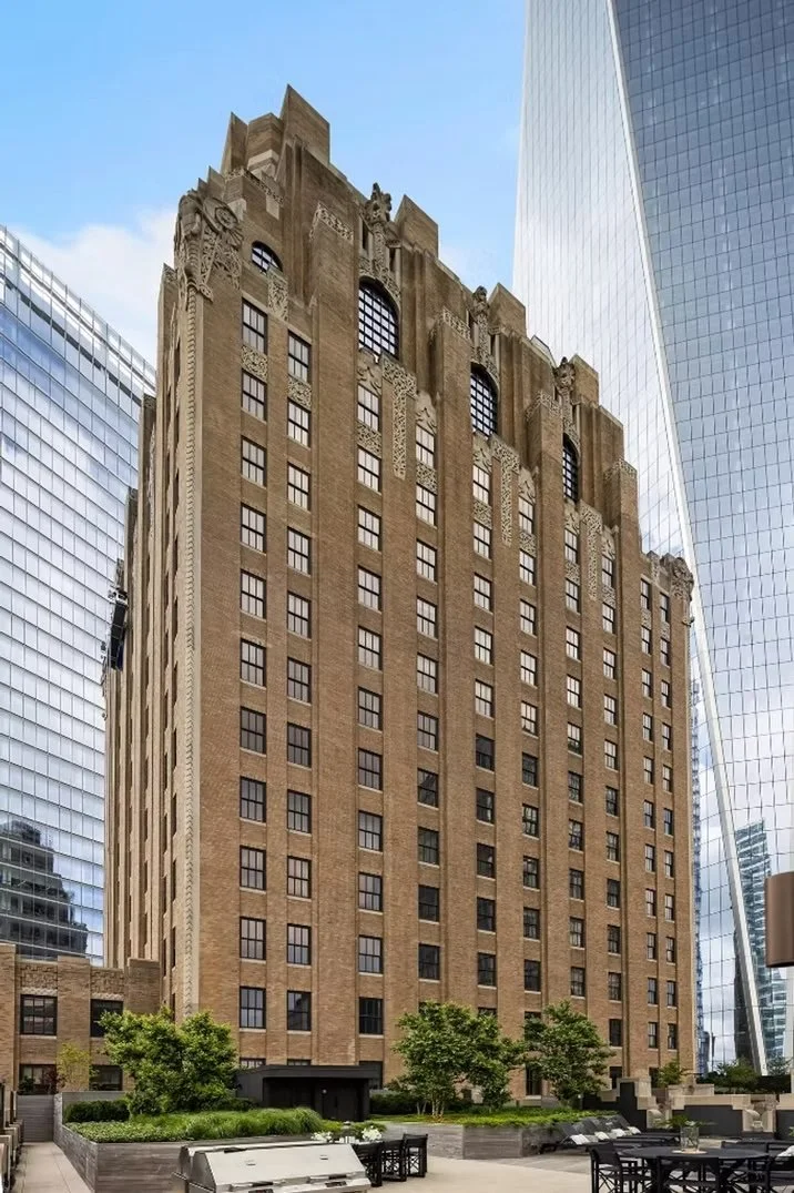 A tall historic building with ornate decorative details on the top, surrounded by modern high-rise glass buildings in an urban downtown area.
