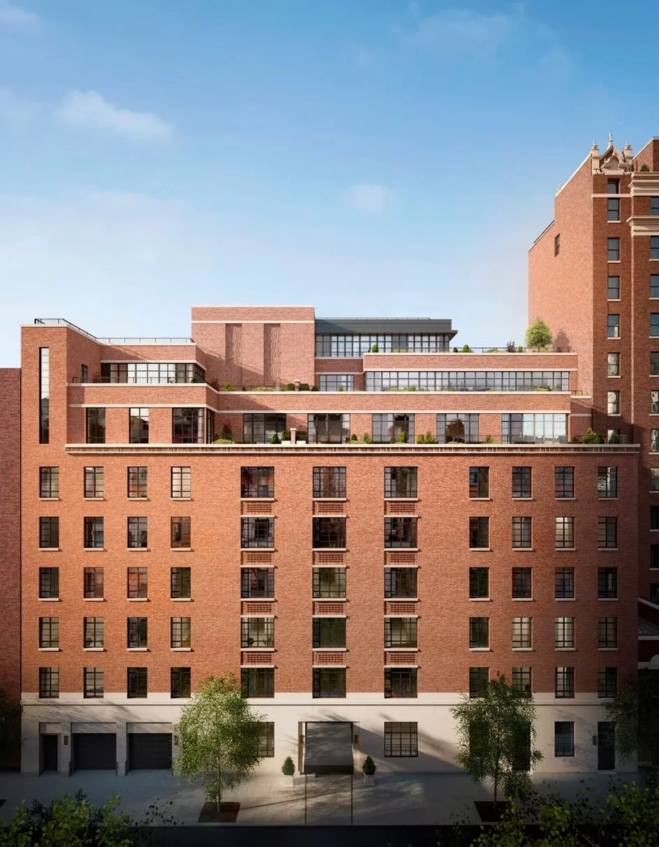 Modern multi-story brick apartment building with large windows and rooftop terraces, with a blue sky and some greenery at street level.