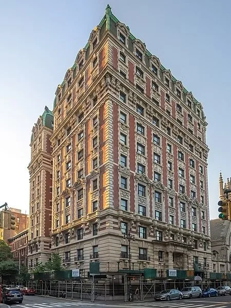 A tall, historic building with ornate architecture, multiple windows, and a green roof, situated on a city street with parked cars.