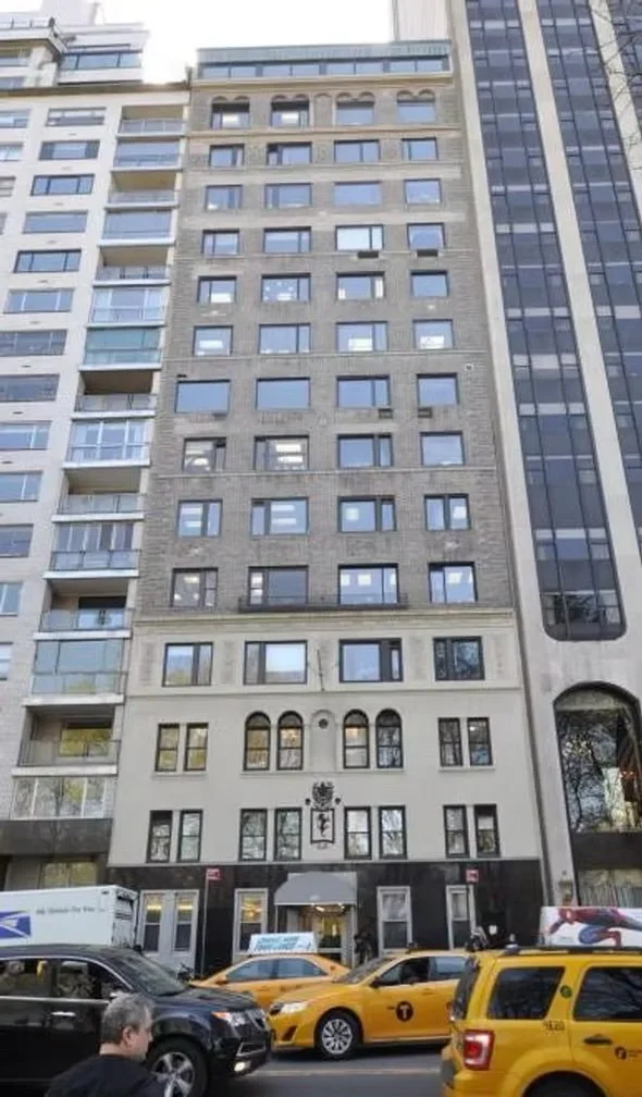 Tall building in an urban city with cars parked in front, including yellow taxis and a postal delivery truck.