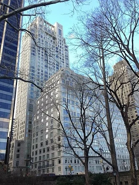 Tall buildings in an urban cityscape with leafless trees in the foreground and a clear blue sky.