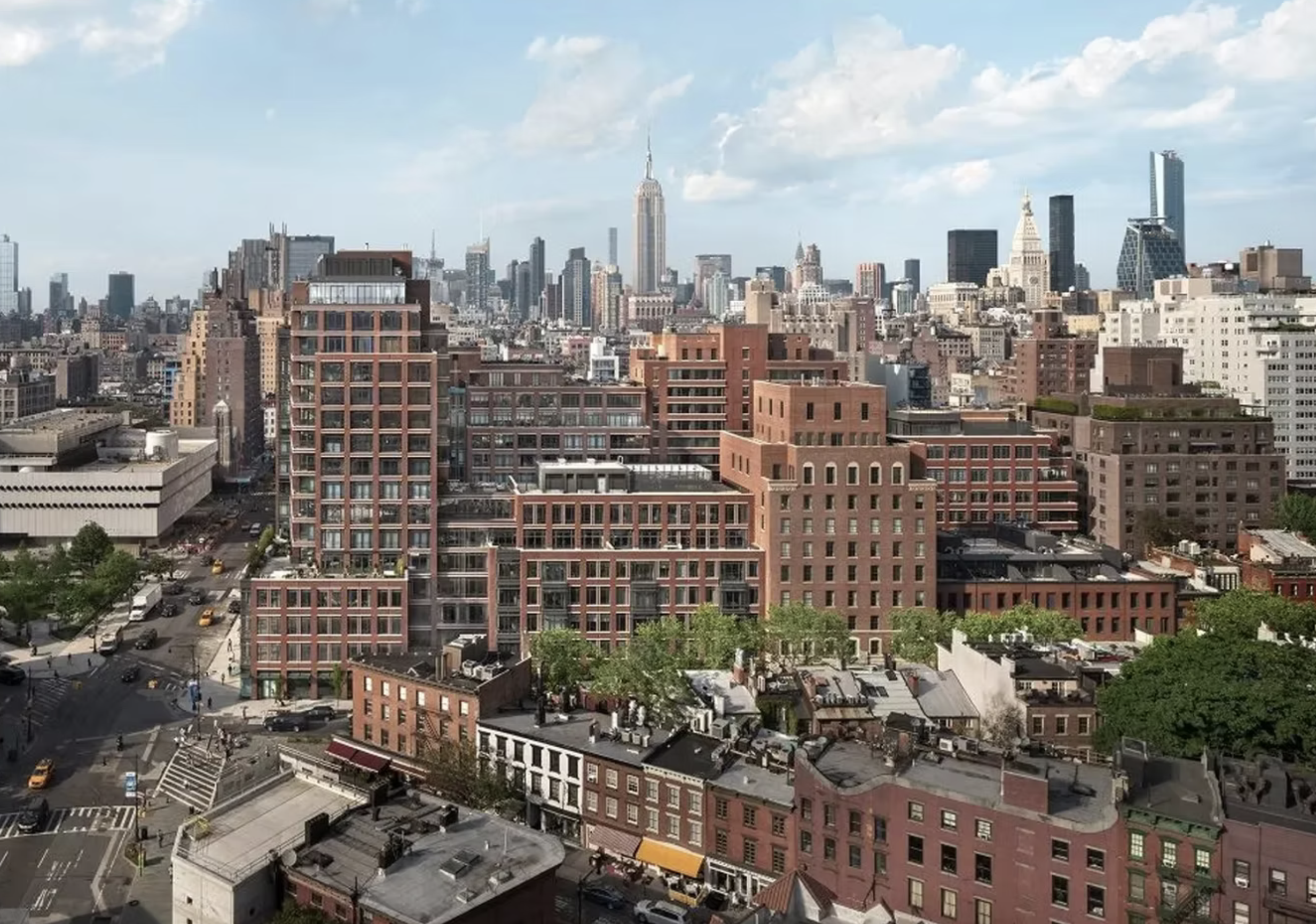 A cityscape featuring tall skyscrapers, mid-rise buildings, and busy streets, with the Empire State Building prominently in the background under a partly cloudy sky.