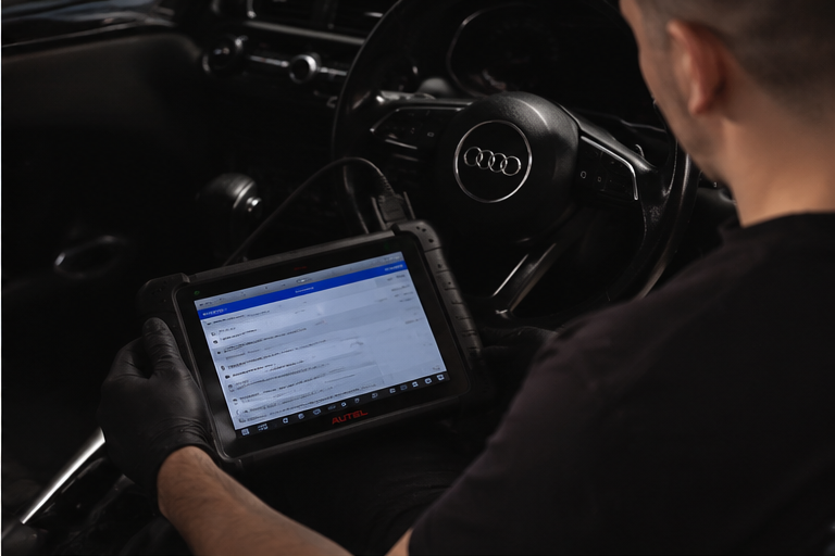 Person wearing black gloves using a diagnostic tablet inside an Audi vehicle.