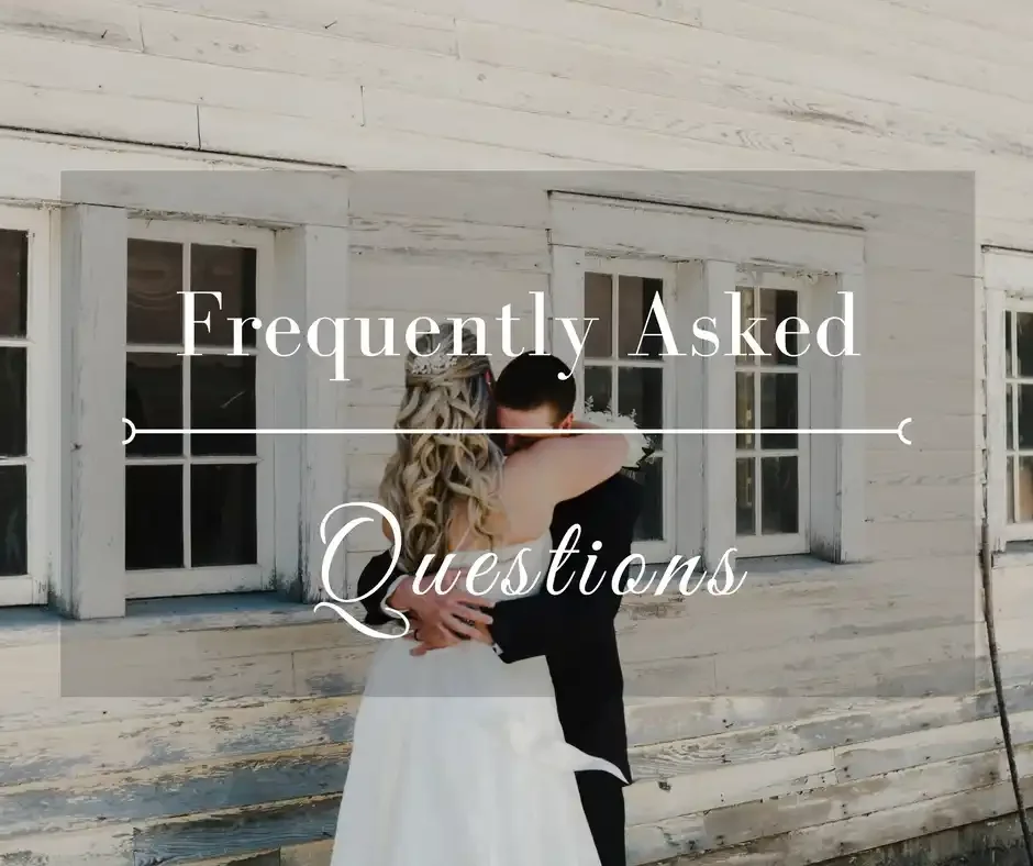 A couple dressed in wedding attire embracing in front of a rustic wooden building with windows.