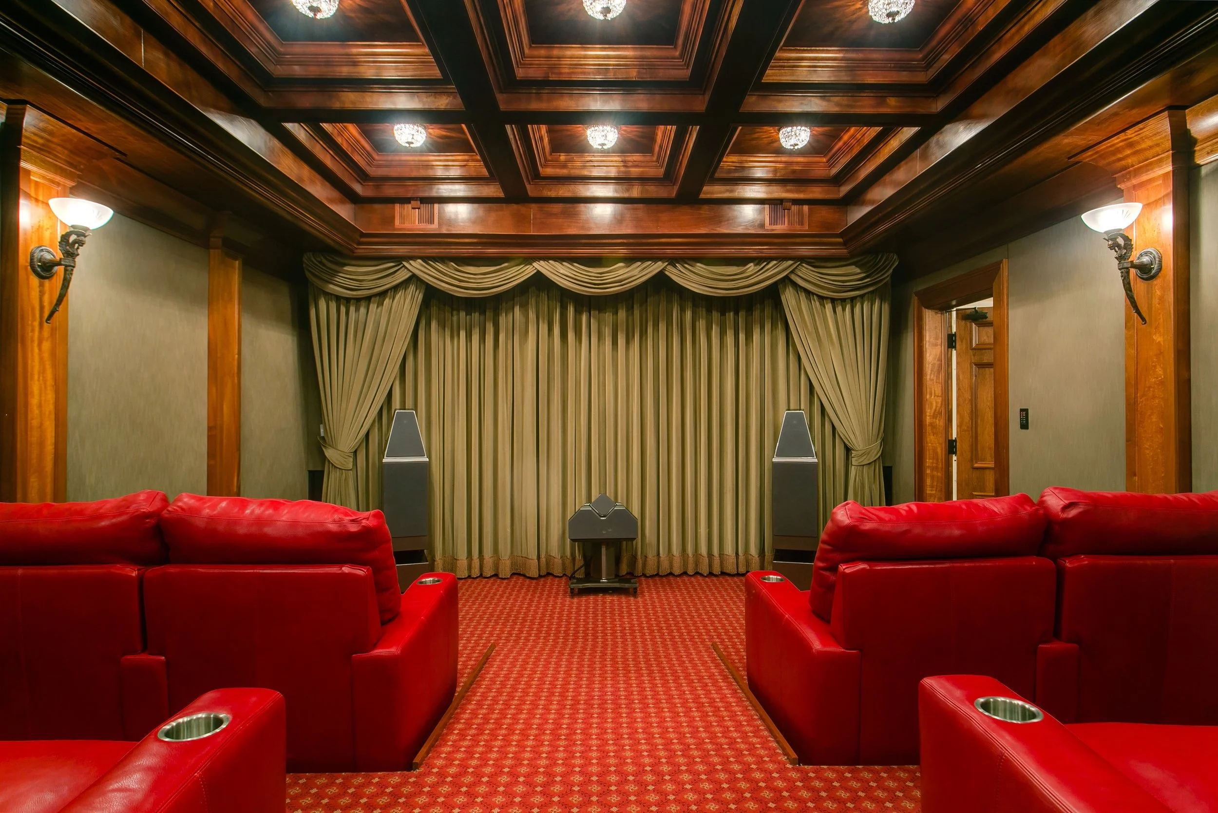 A home theater room with red leather sofas, a large beige curtain covering the back wall, and a wooden coffered ceiling with recessed lighting.