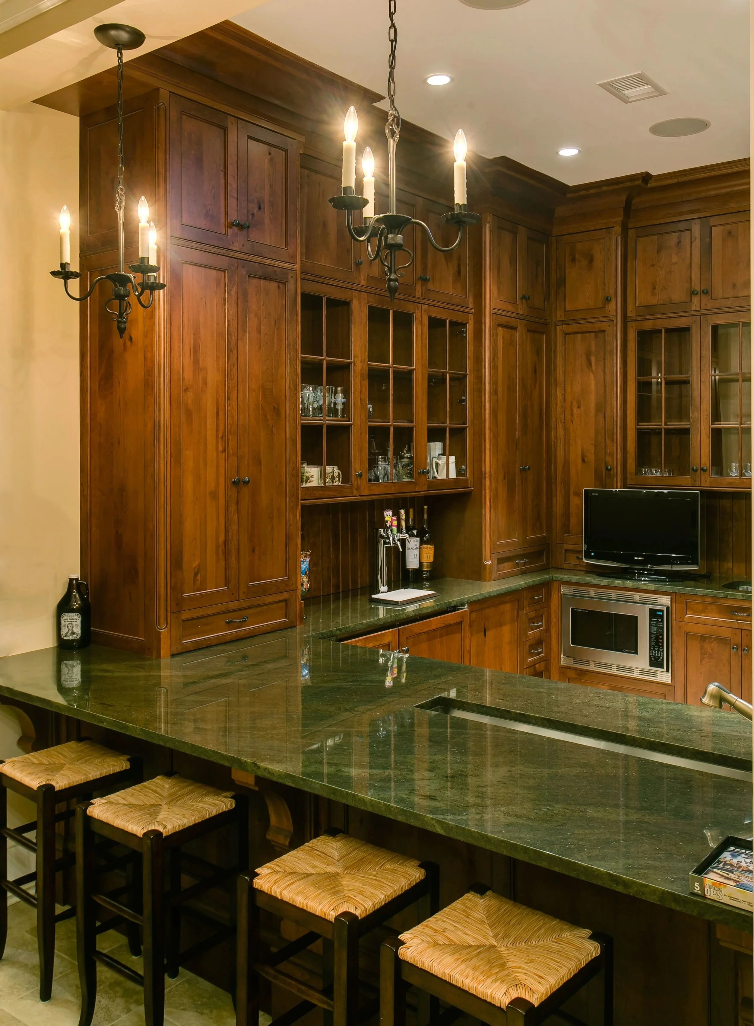 Kitchen with wooden cabinets, a green stone countertop, a black television, a microwave, and a chandelier with candles hanging from the ceiling.