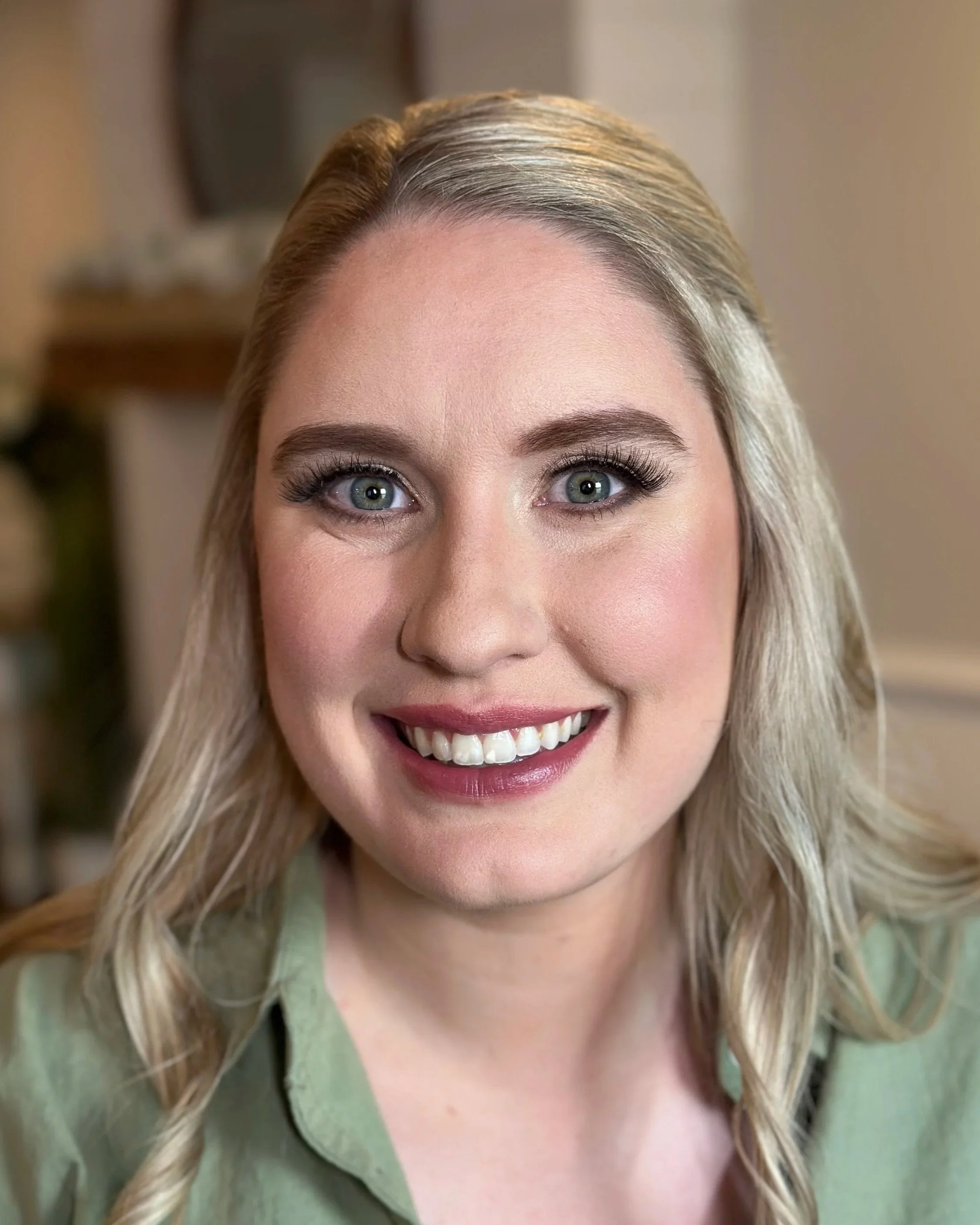 Close-up of a smiling woman's face, showing her blue eyes, blonde hair, and makeup.