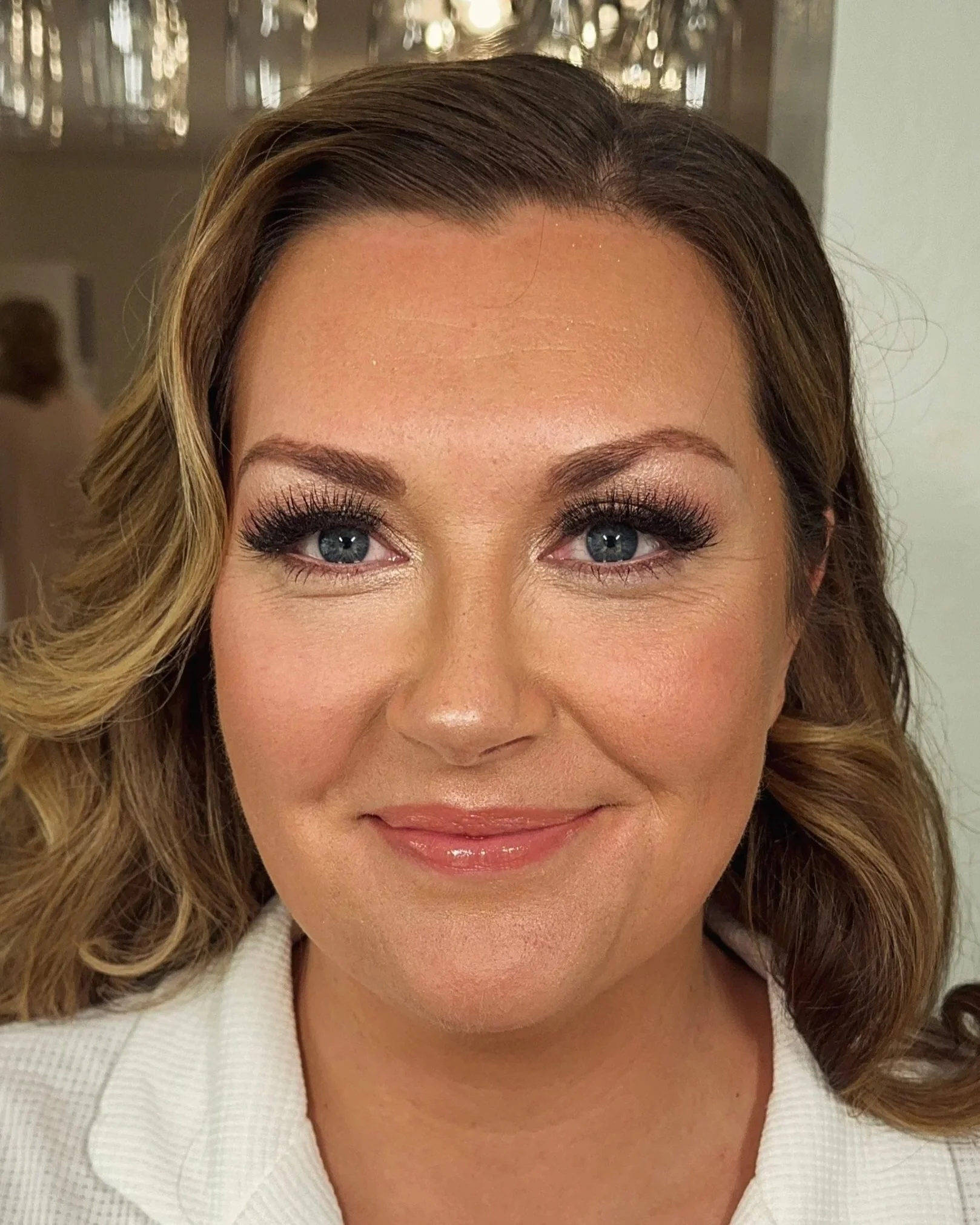 Close-up of a woman's face showing her eyes, eyebrows, and smile, with curly light brown hair and wearing a white garment.