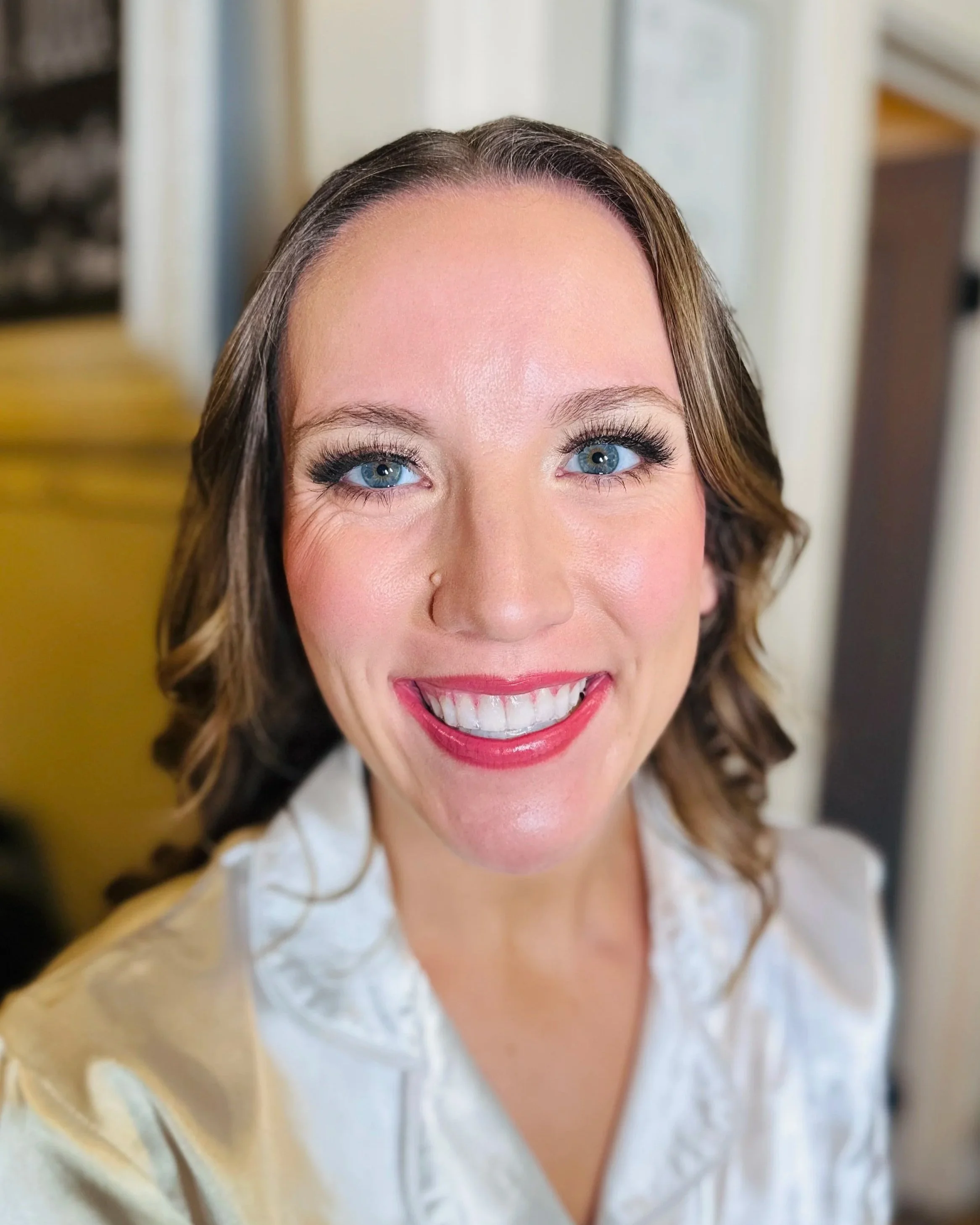 Close-up of a smiling woman with blue eyes, wearing makeup, and curly hair, in a white blouse.