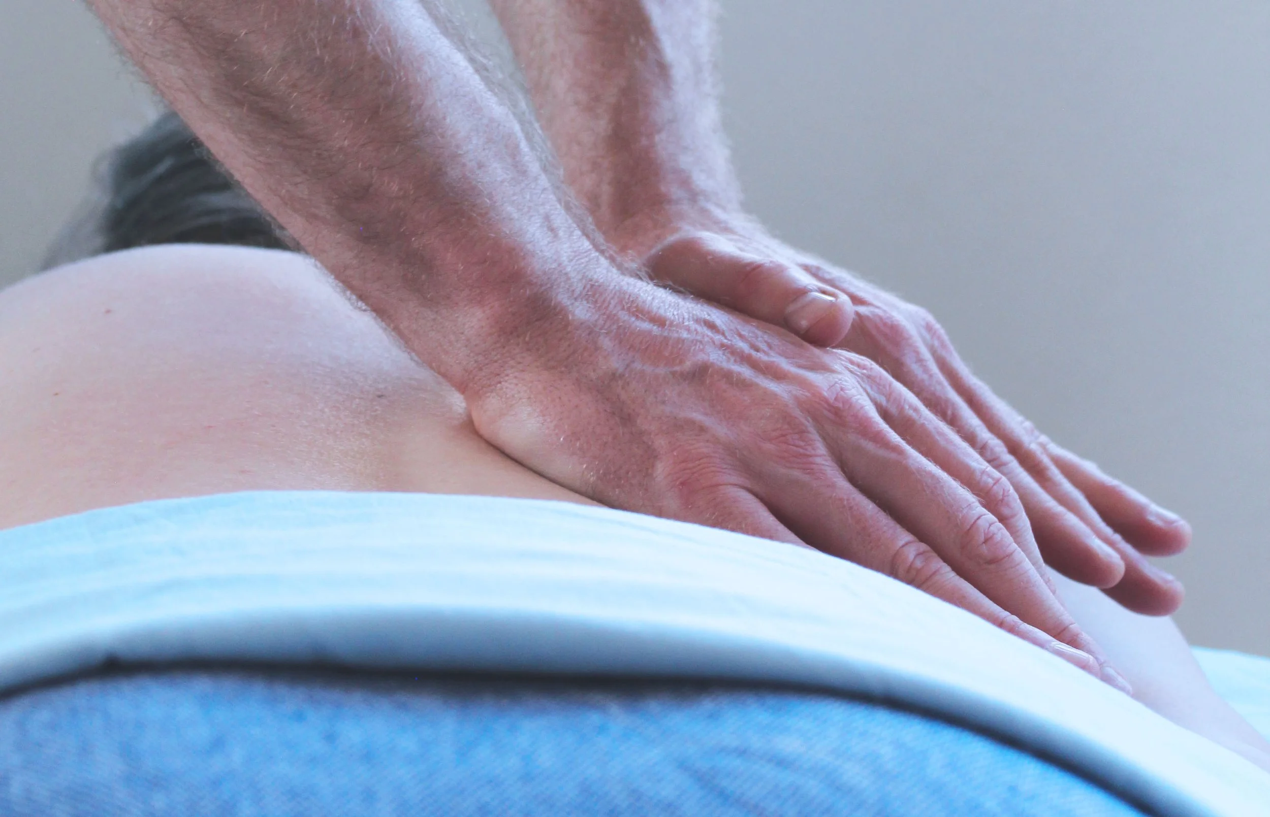 Close-up of a person's hand applying pressure during a massage on a person with light skin, wearing a light blue garment.