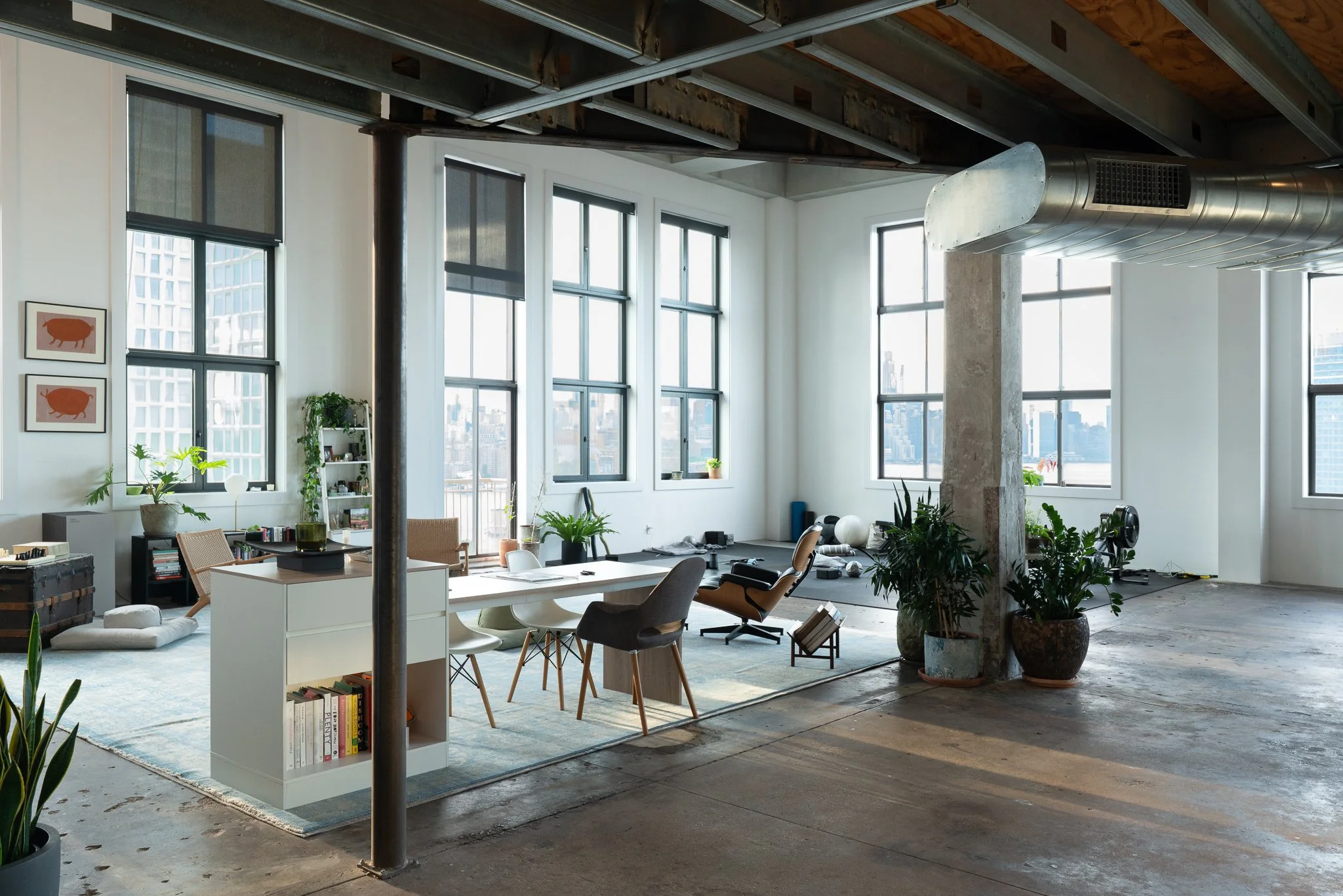 Modern loft apartment with large windows, plants, and contemporary furniture, under construction or renovation with exposed ceiling beams and ductwork.